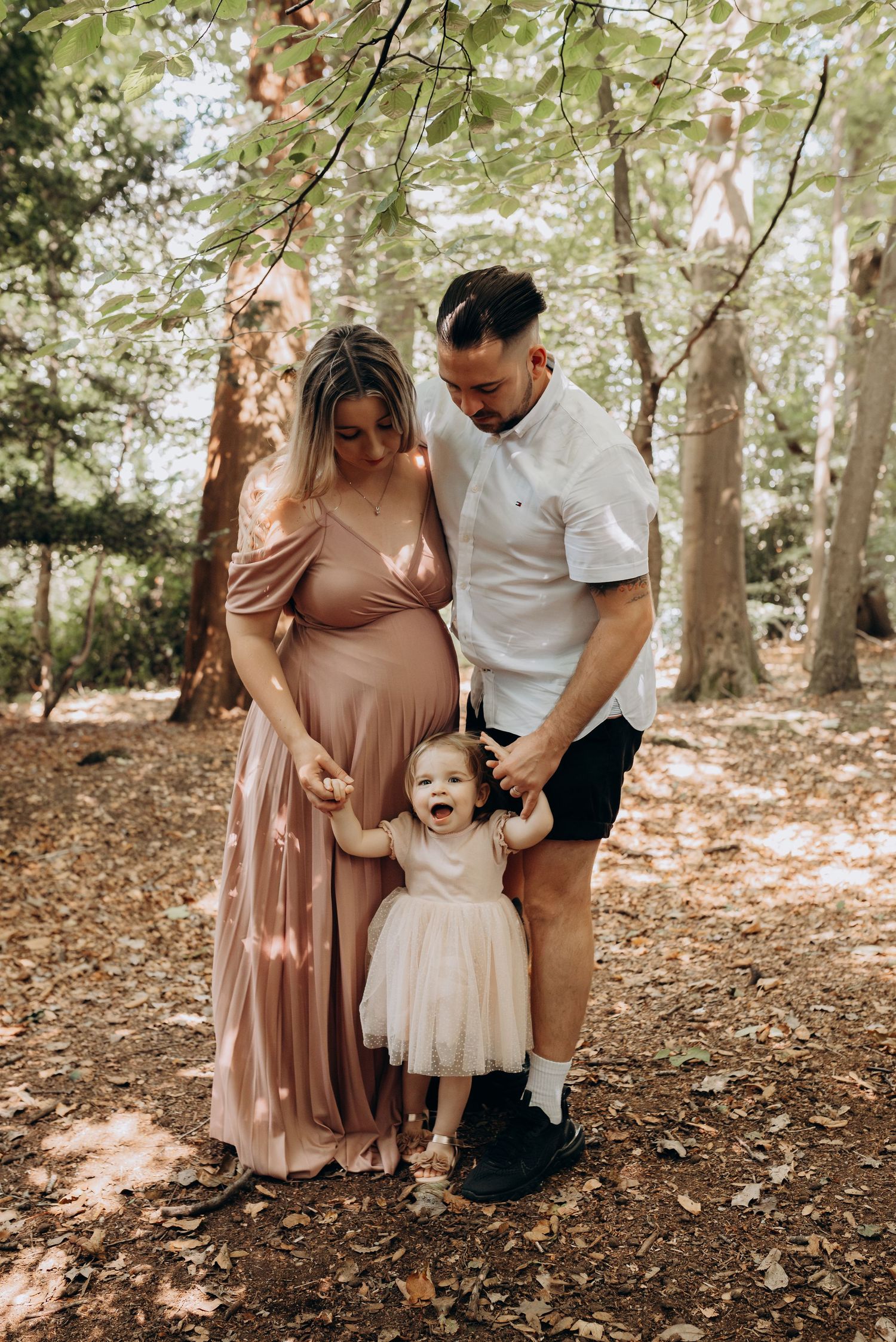 A family shares joyful moments together in a wooded forest setting wearing coordinated neutral tones.