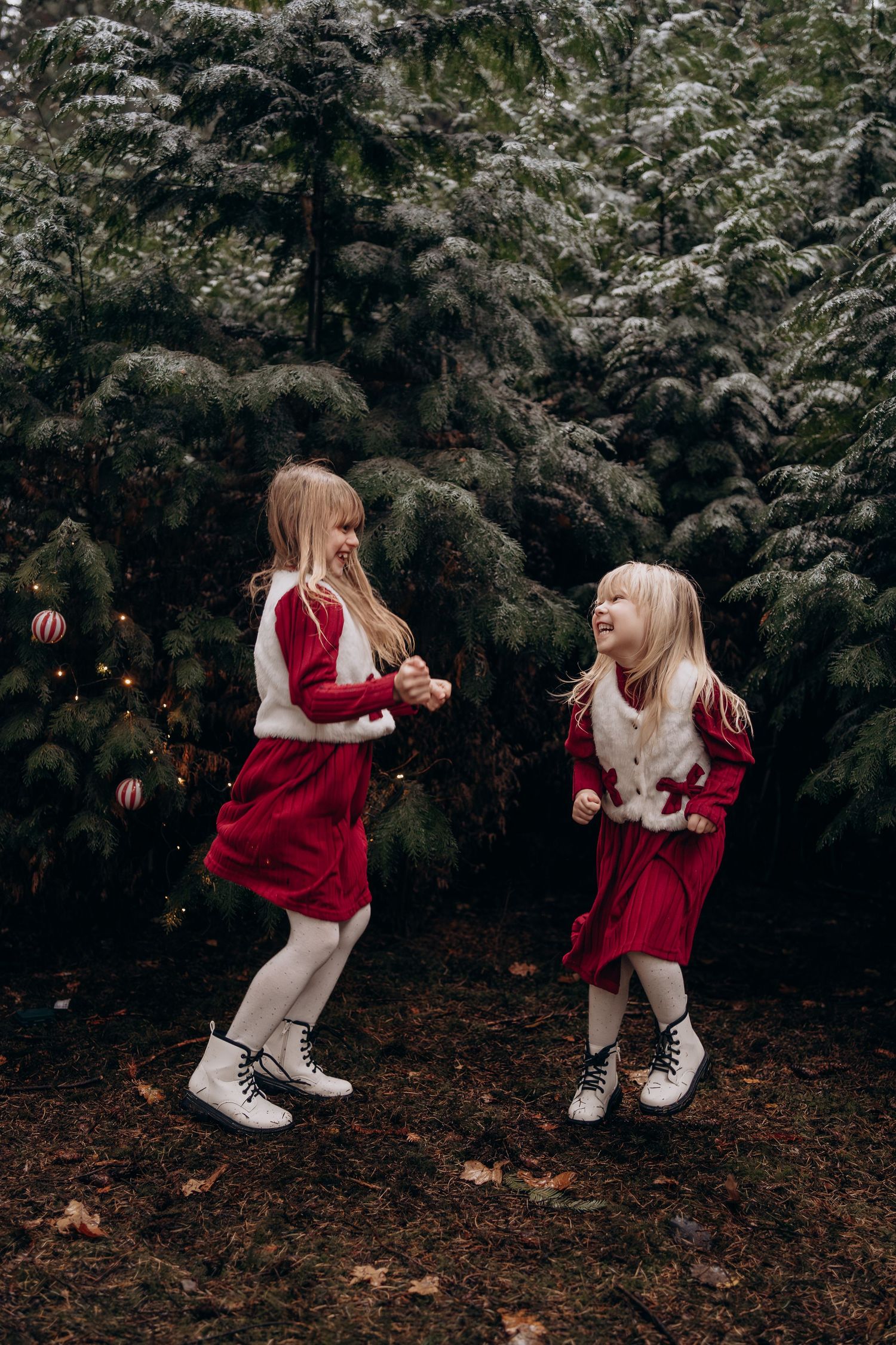 A couple in red sweaters share a tender moment while kneeling on fallen autumn leaves in a forest setting.