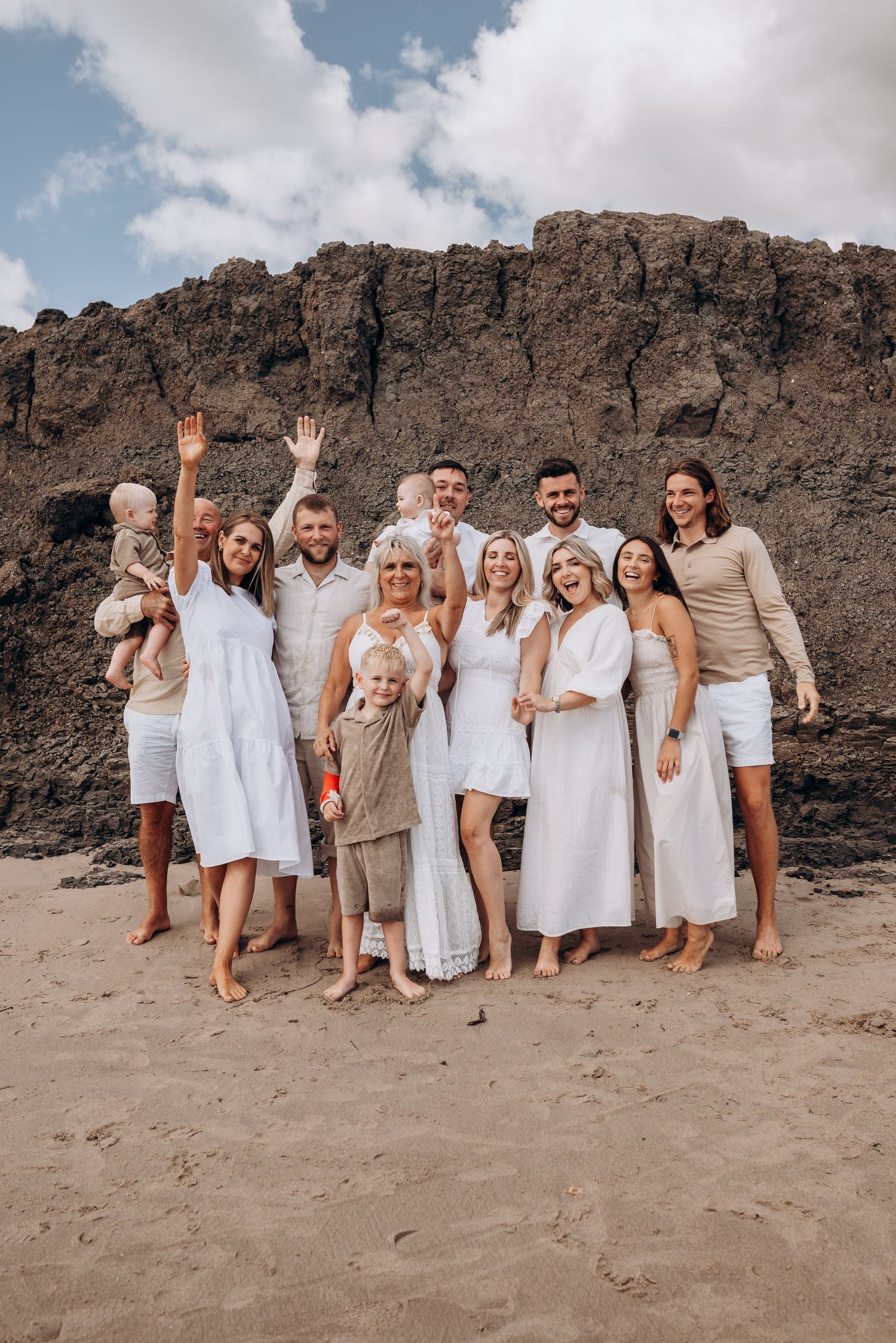 A large family group poses for a photo on a beach with dramatic cliffs in the background.