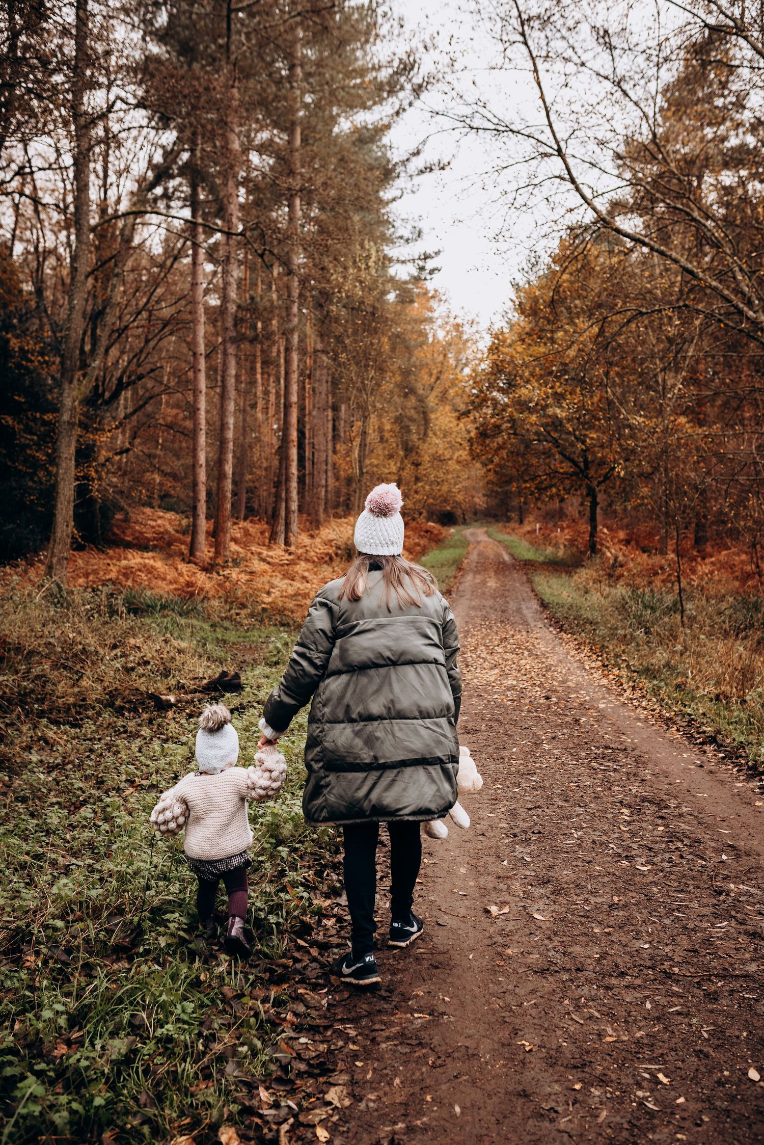 Two people walk along an autumn forest trail surrounded by golden foliage.