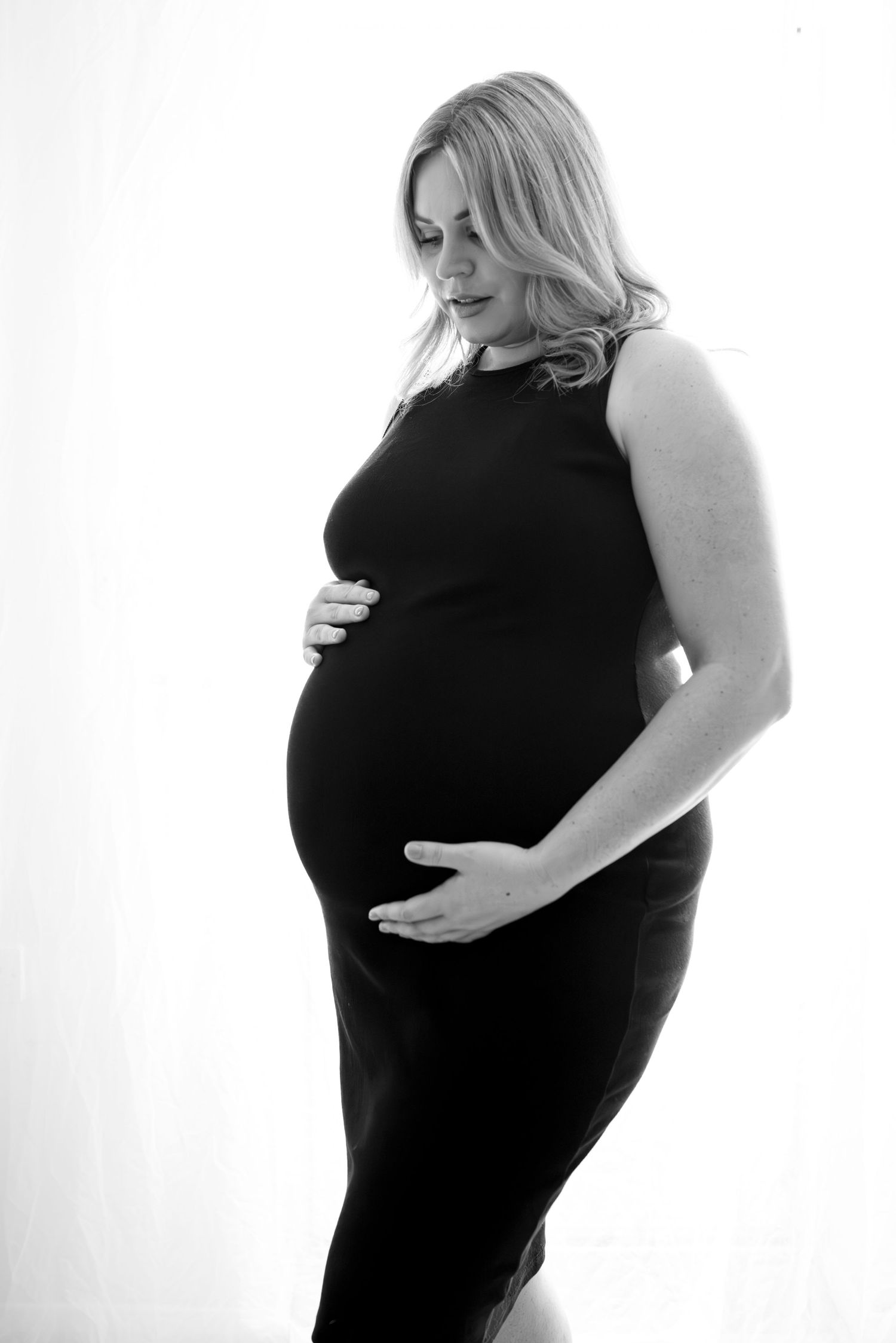 Black and white maternity portrait showing silhouette in fitted black dress.