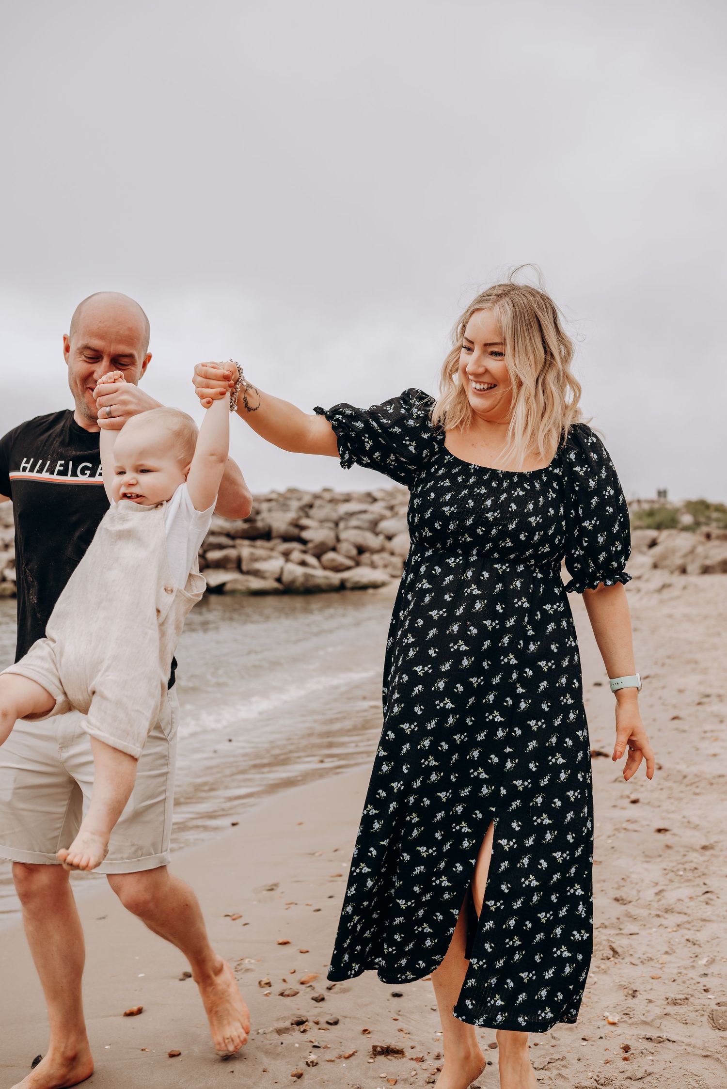 A family walks together on a rocky beach holding hands.