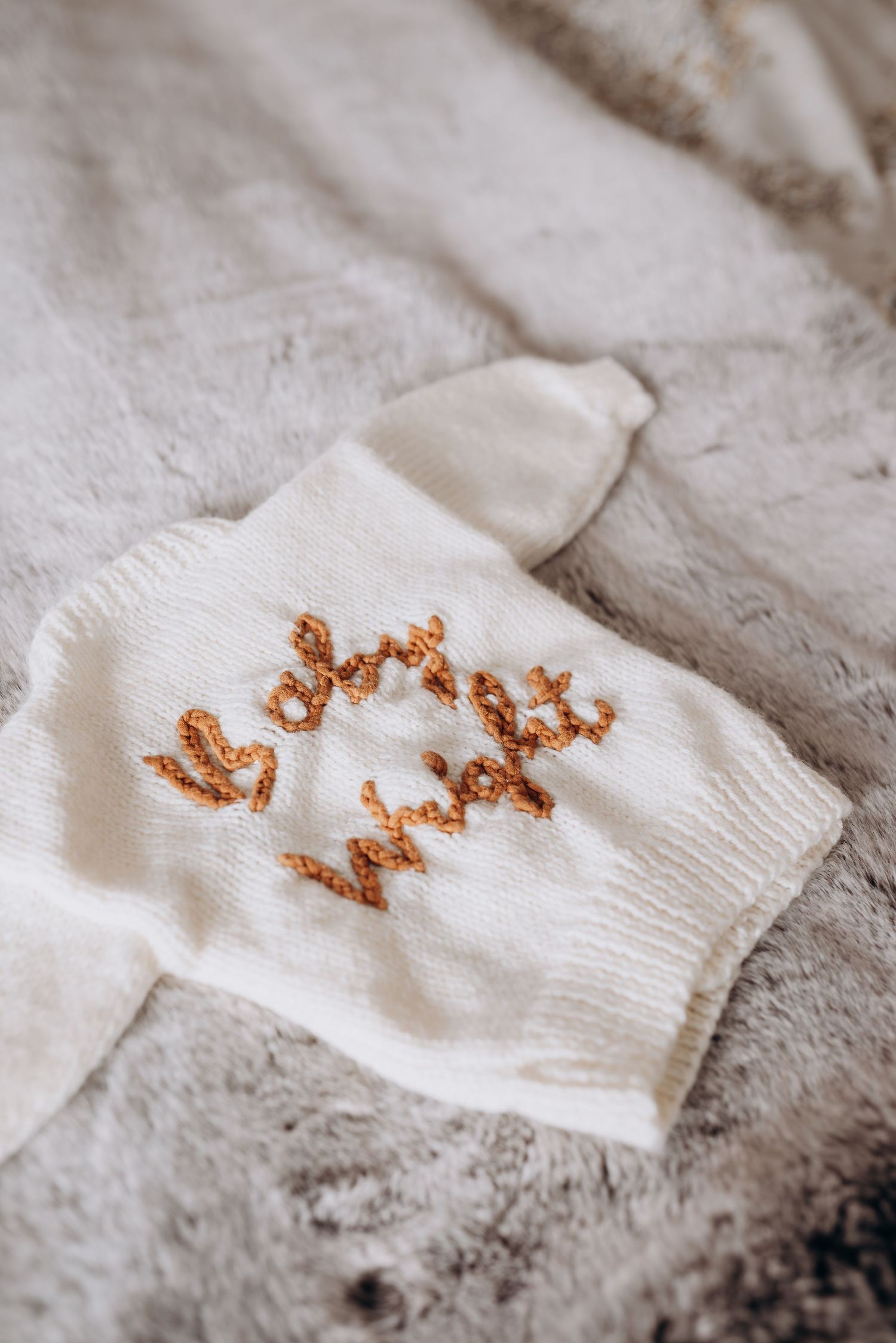 White knit fabric with orange embroidered text visible in a close-up detail shot.