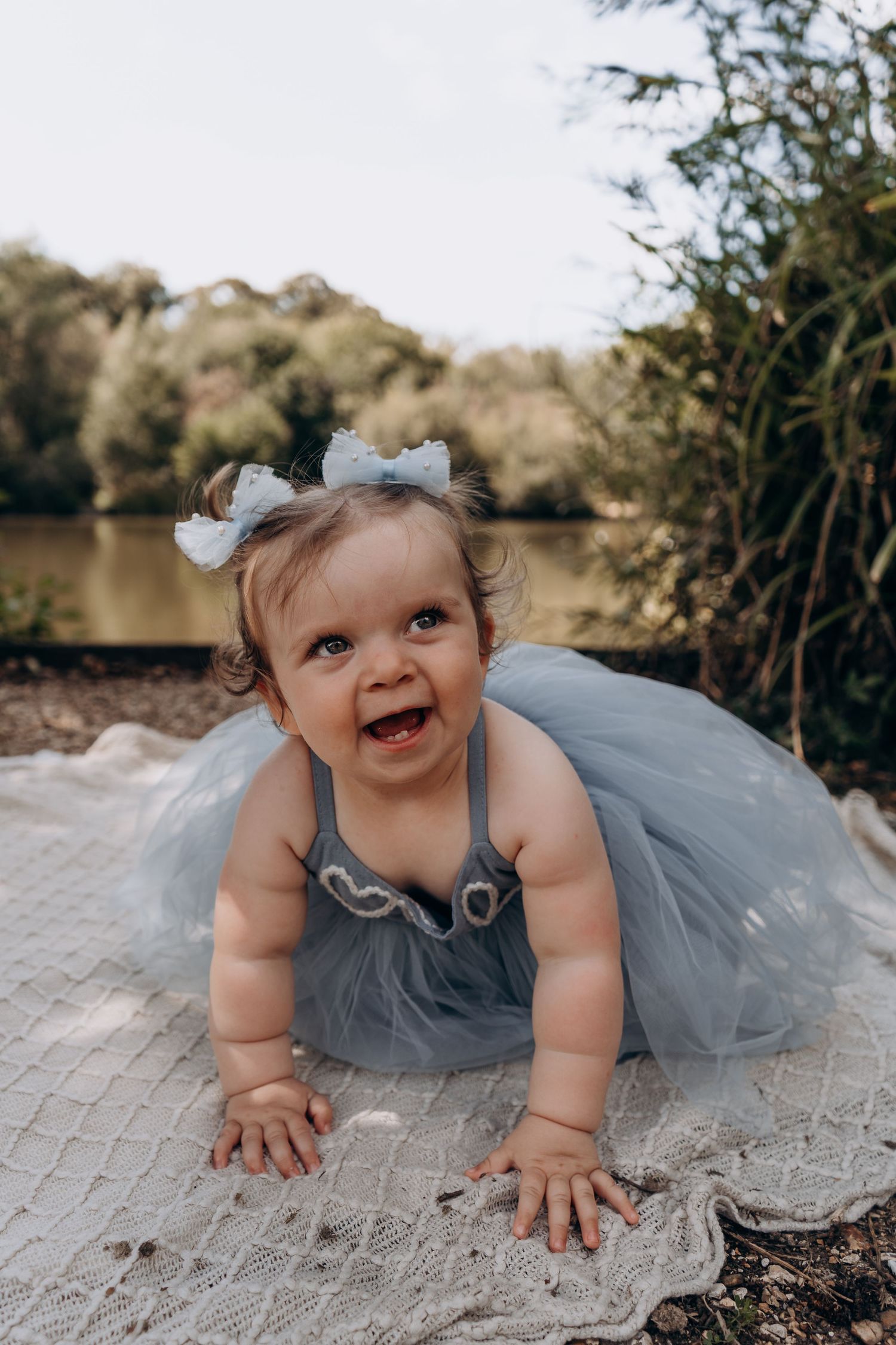 A baby wearing a gray tulle dress crawls on a stone surface outdoors.