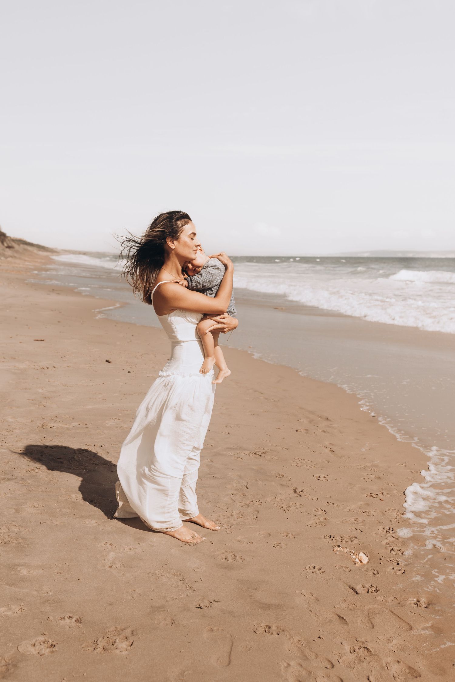 Woman in flowing white dress twirling joyfully on sandy beach.