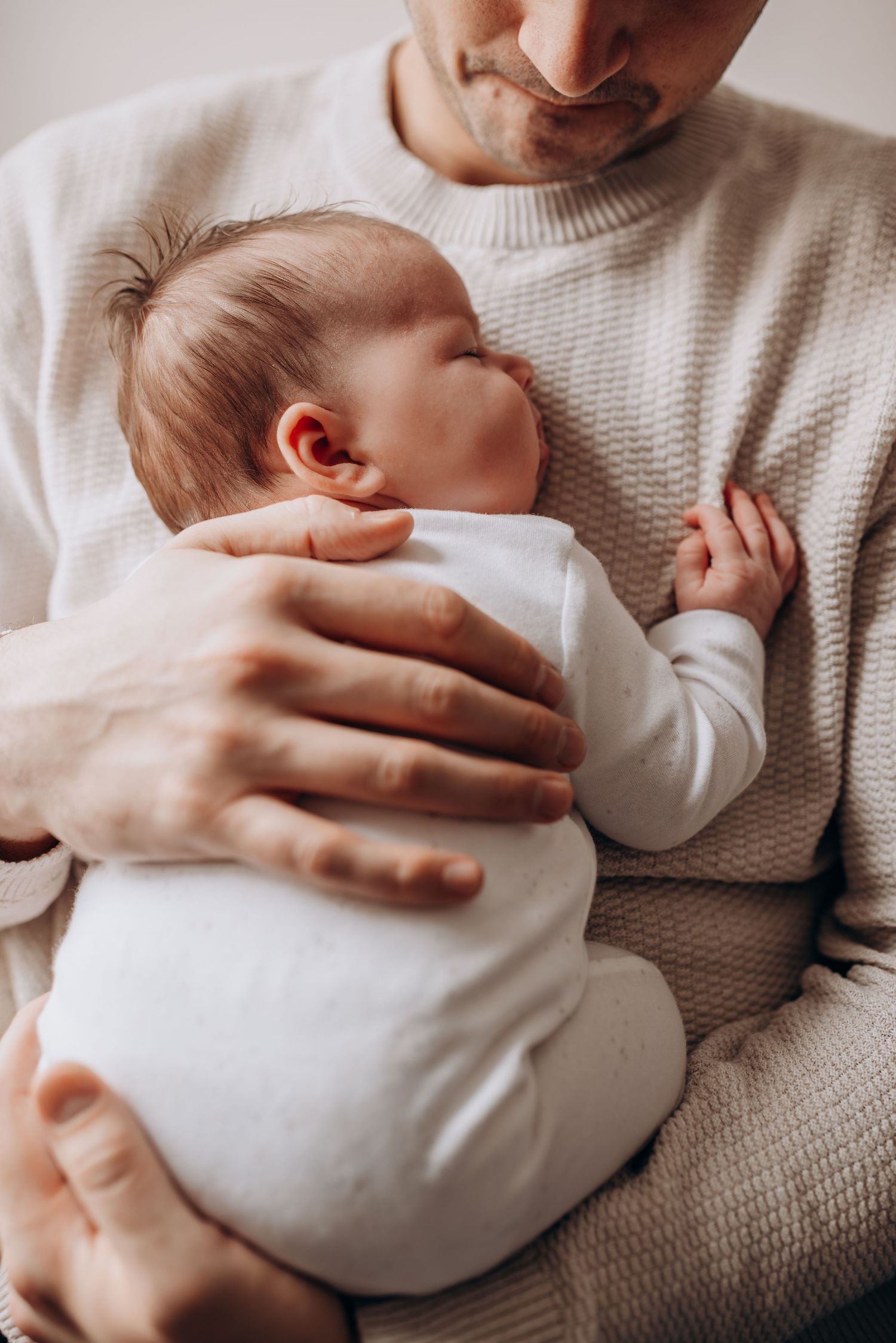 Close-up shots of gentle hands cradling a newborn baby wrapped in white.