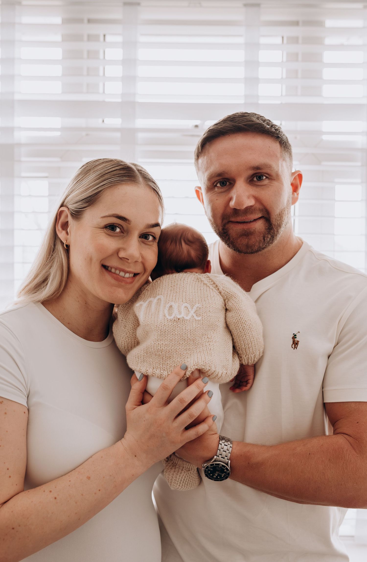 A family of three poses together by a bright window, sharing tender moments with their newborn.