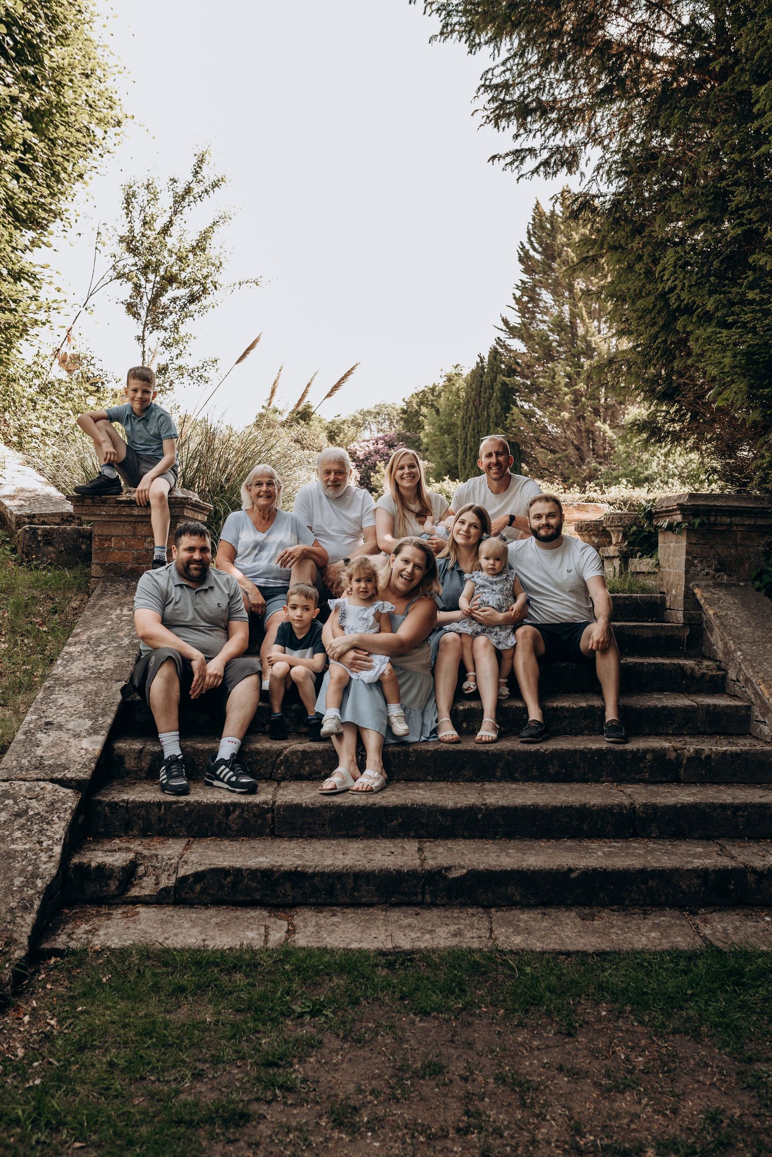 A large group sits together on outdoor stone steps during a casual outdoor photoshoot.