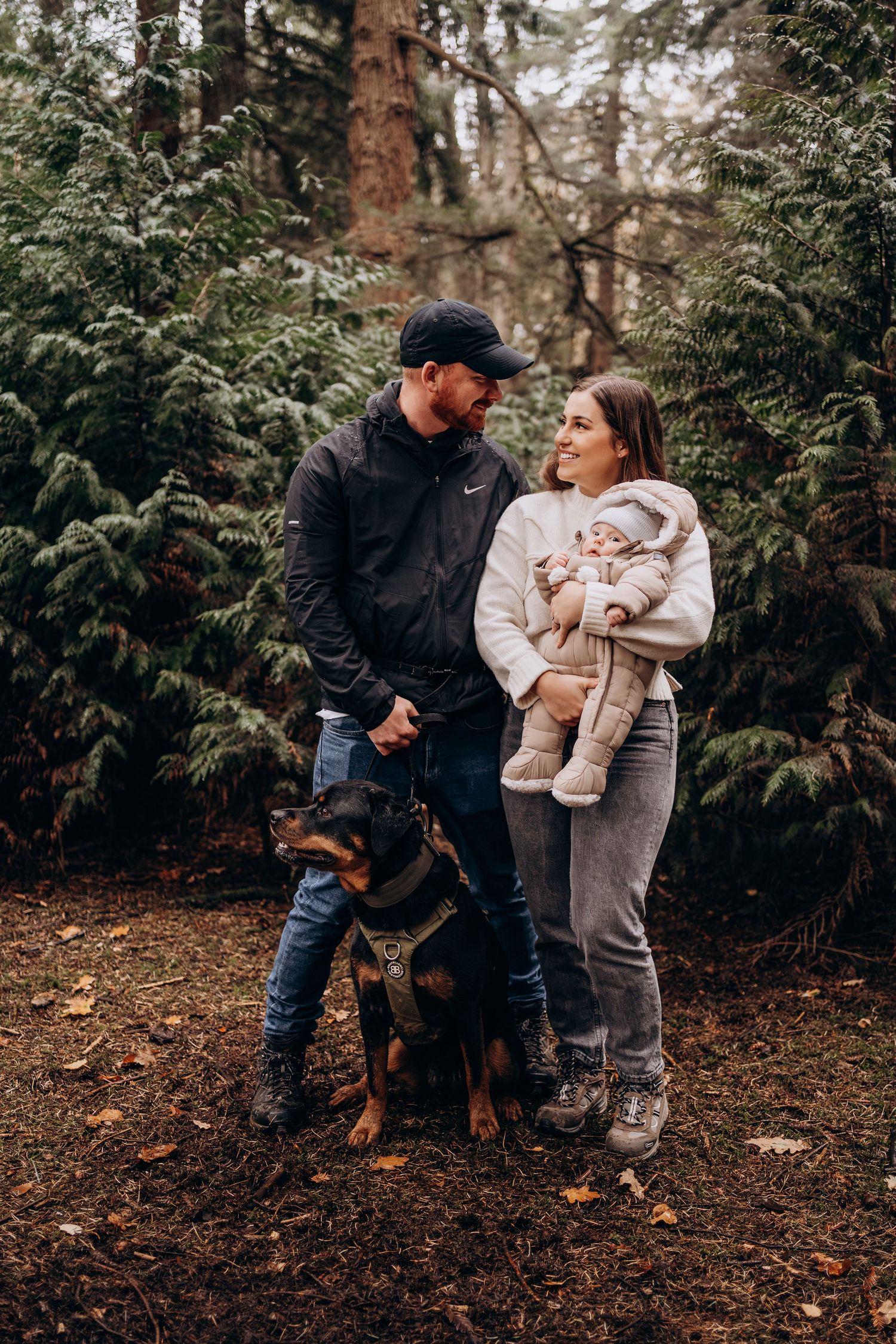 A couple and their dog share tender moments in a wooded forest setting during an autumn photoshoot.
