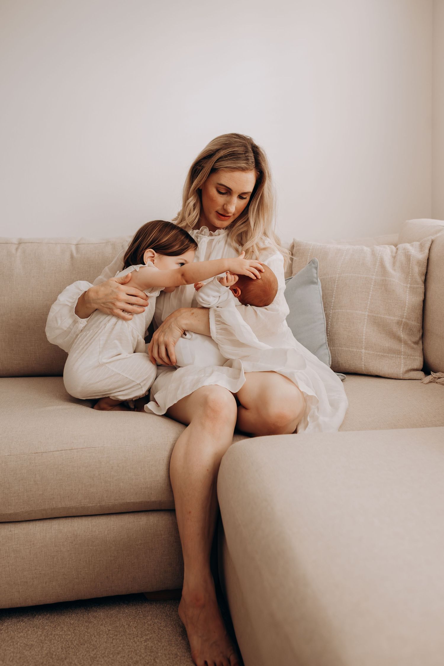 Mother and baby sharing intimate moments on beige couch in natural lighting.