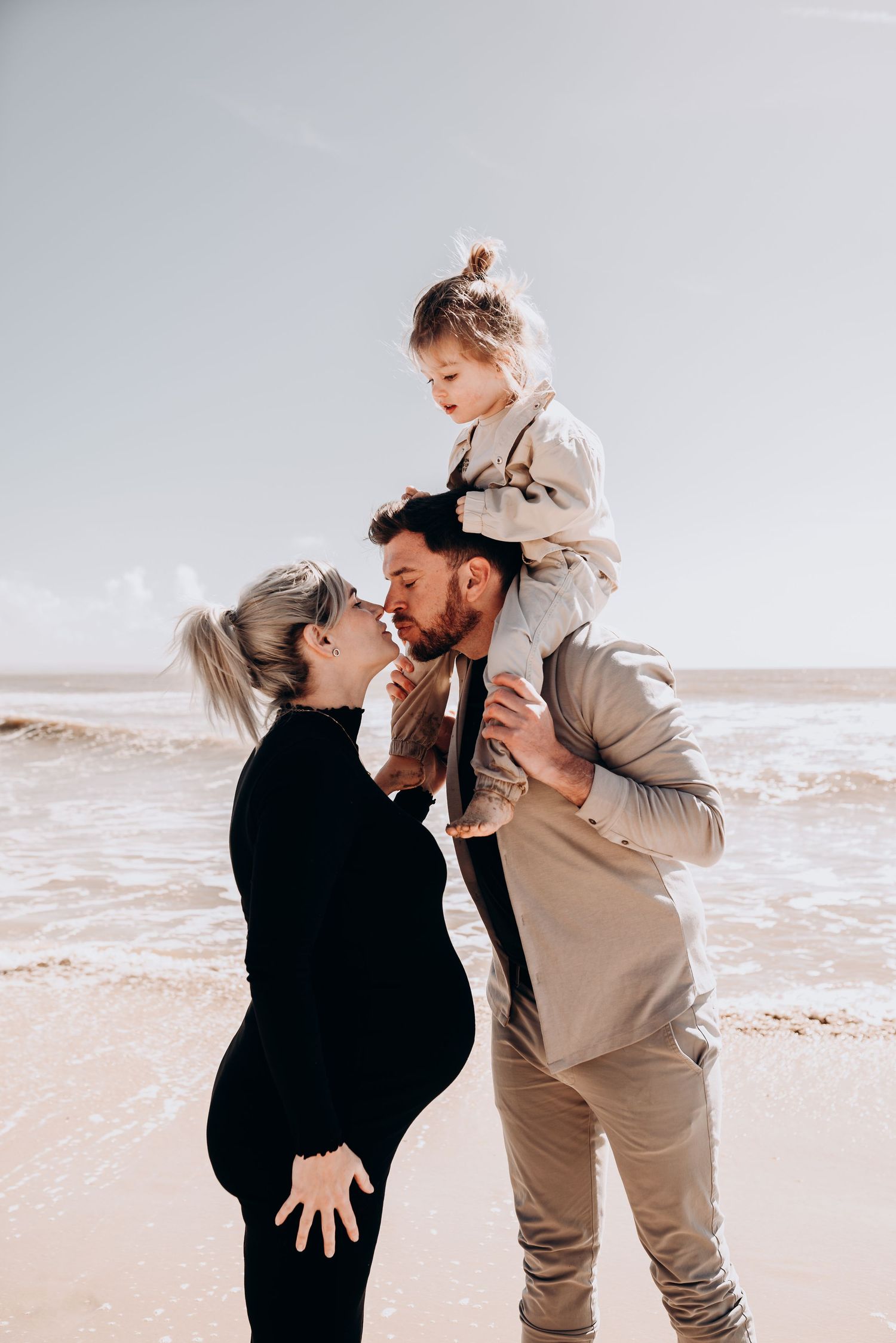 Family of three sharing joyful moments together on beach in casual attire.