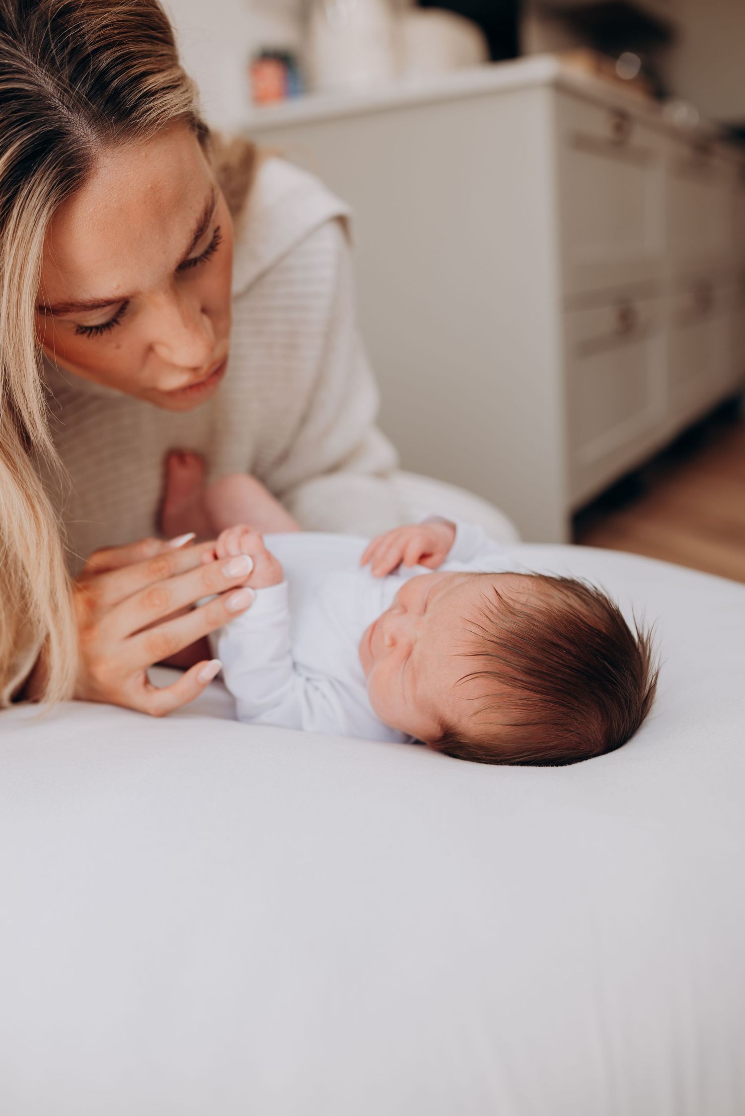 A gentle moment captured as someone leans over to observe a sleeping newborn on white bedding.