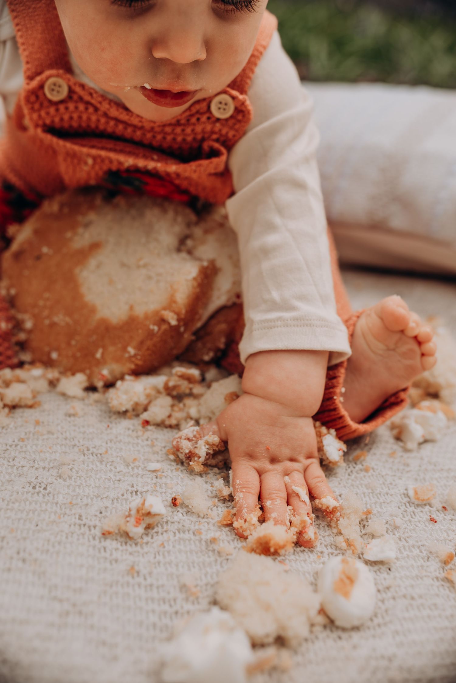 Close-up of small hands playing with cake crumbs during first birthday celebration.