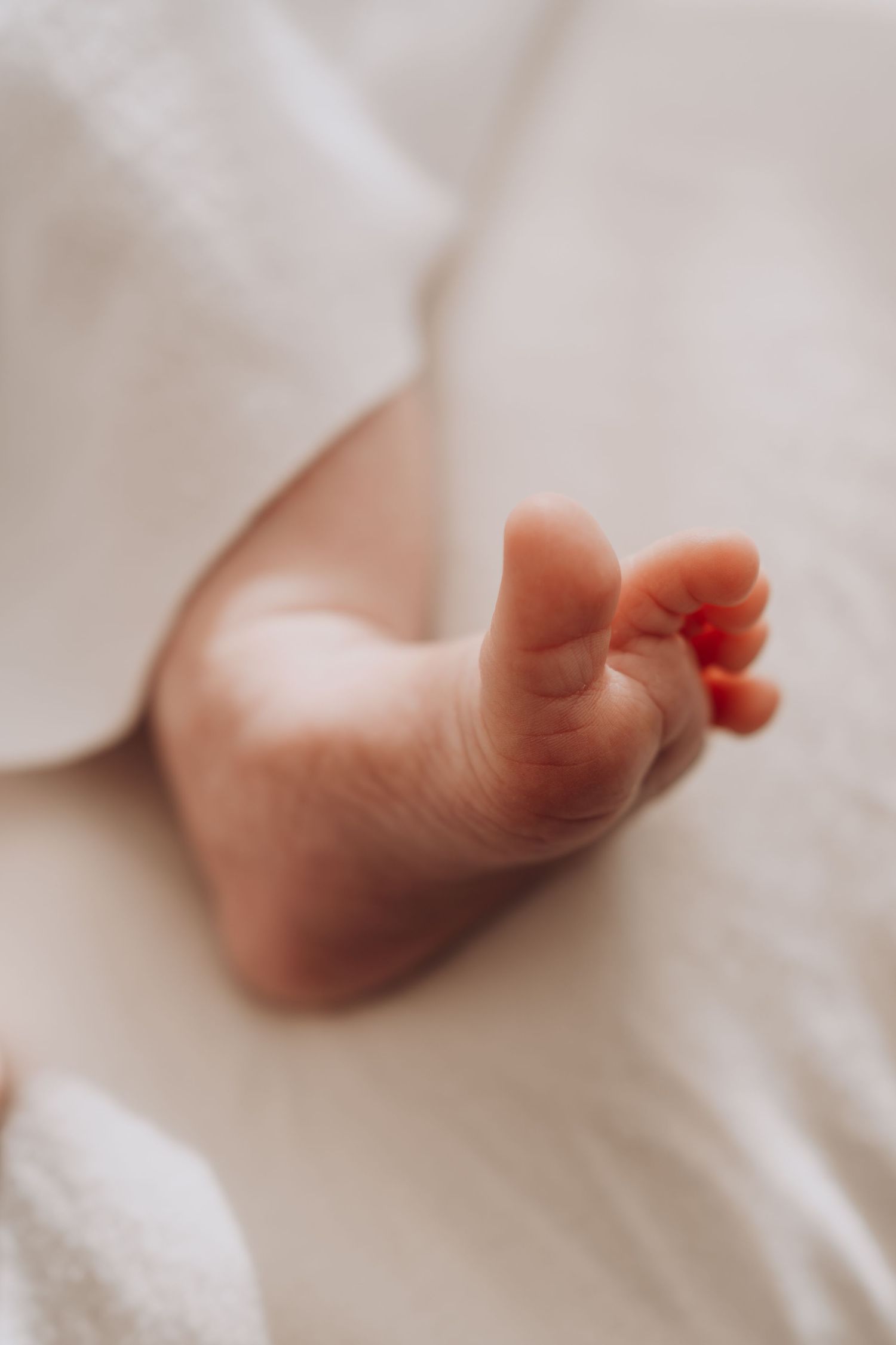 Baby's tiny feet peeking out from under white blanket.