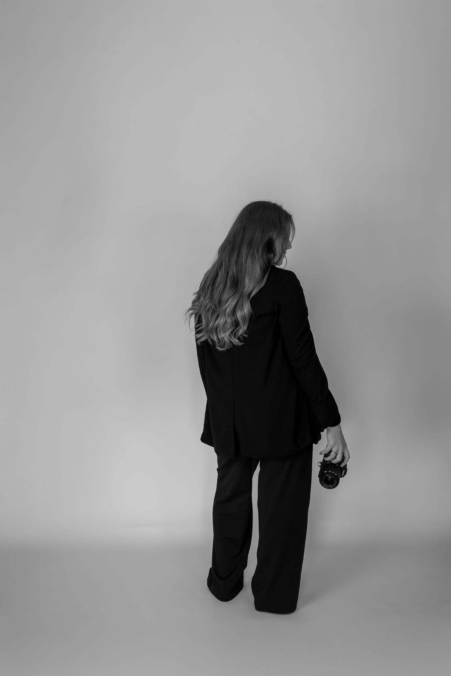 A figure in black clothing bends forward in a dramatic pose against a light gray background.