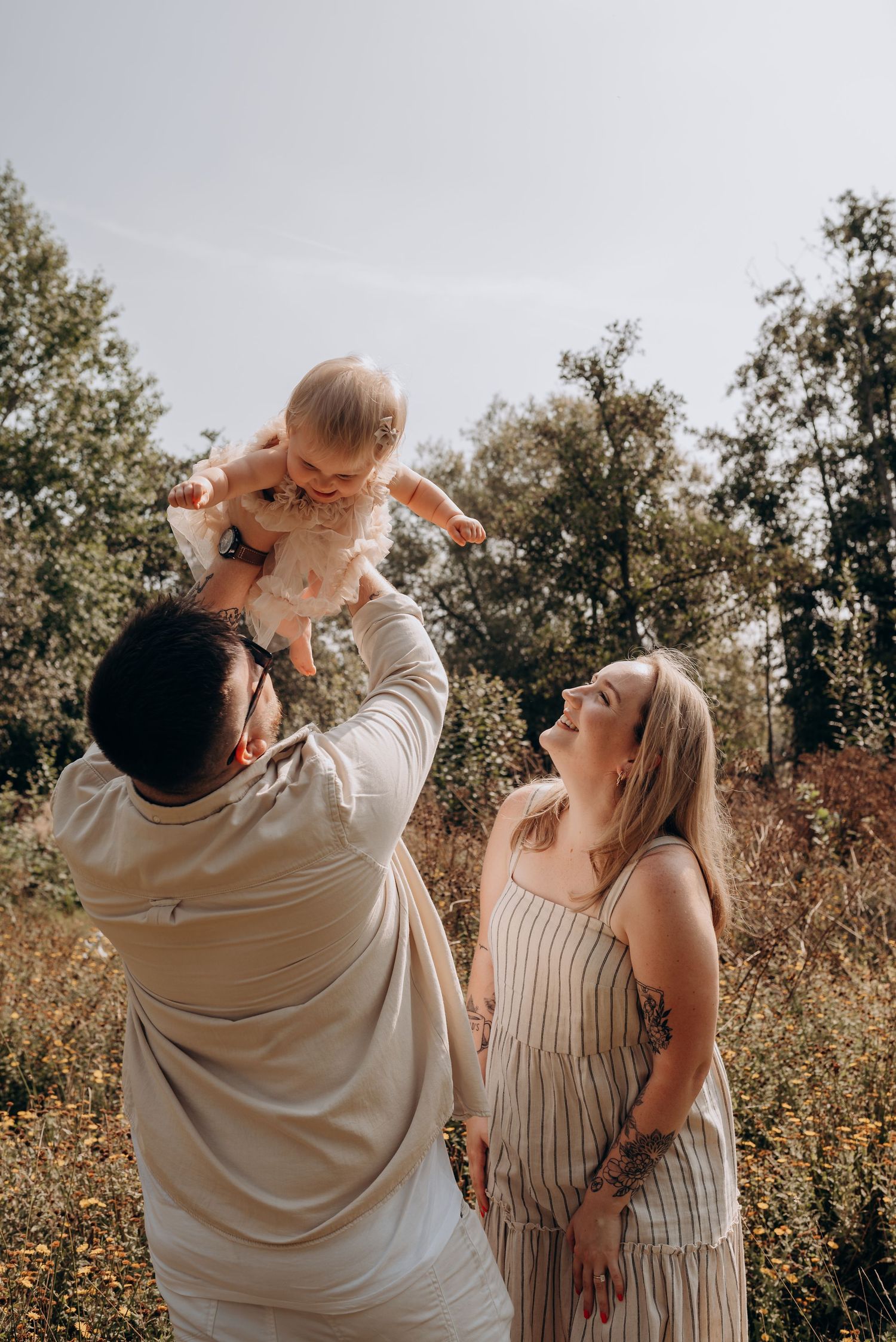 A family shares a joyful moment outdoors with their baby in a natural setting.
