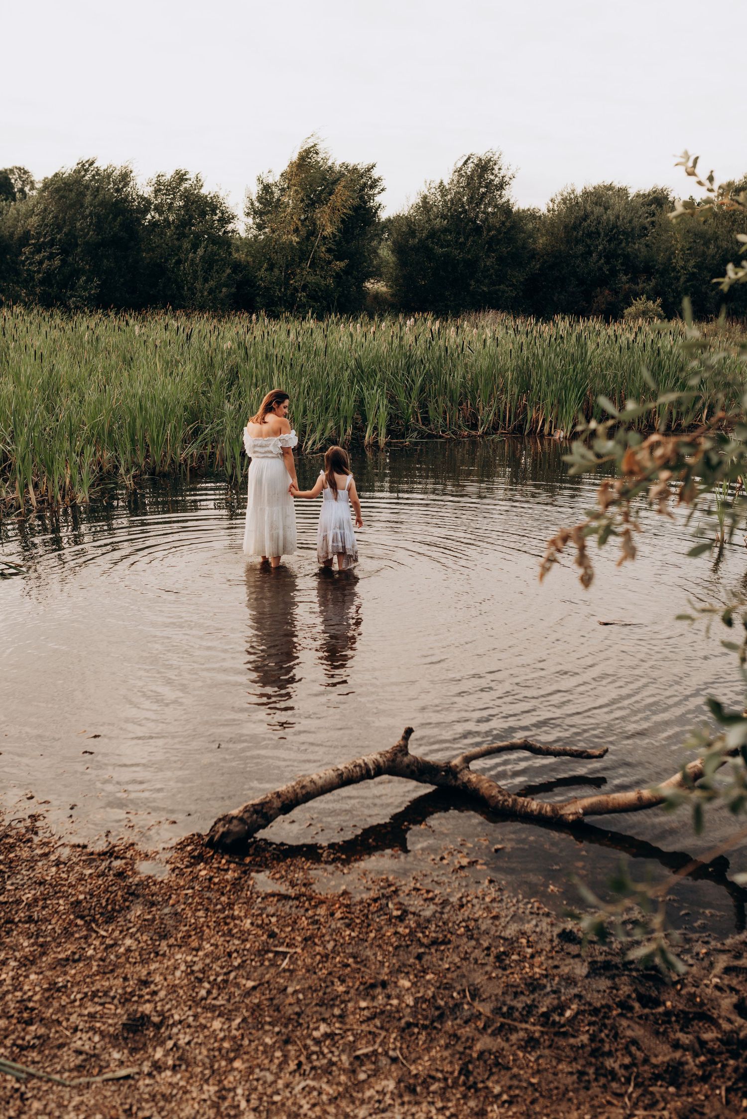 Couple embracing in a serene lake surrounded by tall reeds and natural scenery at sunset.