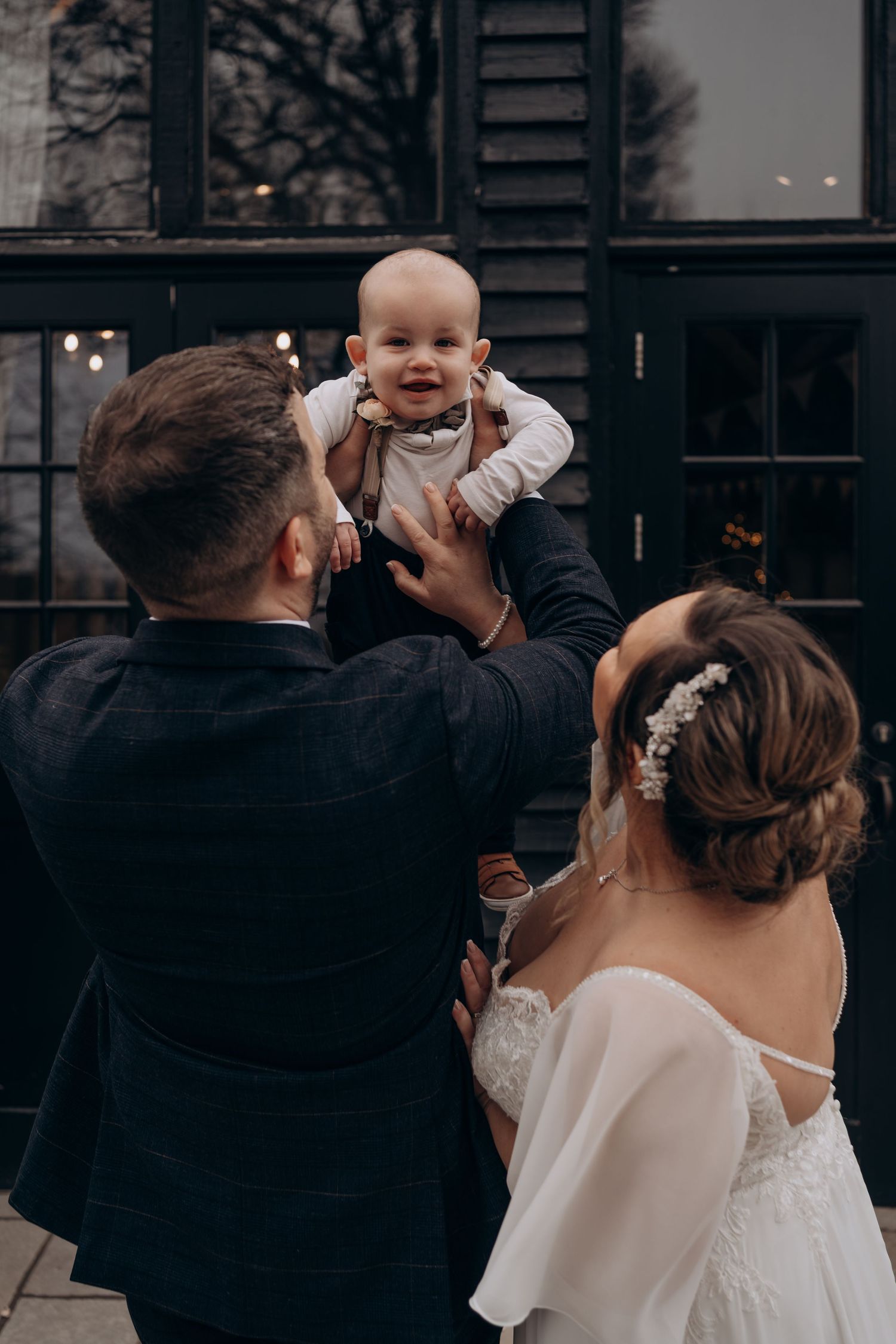 A couple in wedding attire shares a tender moment with a baby at an outdoor venue.