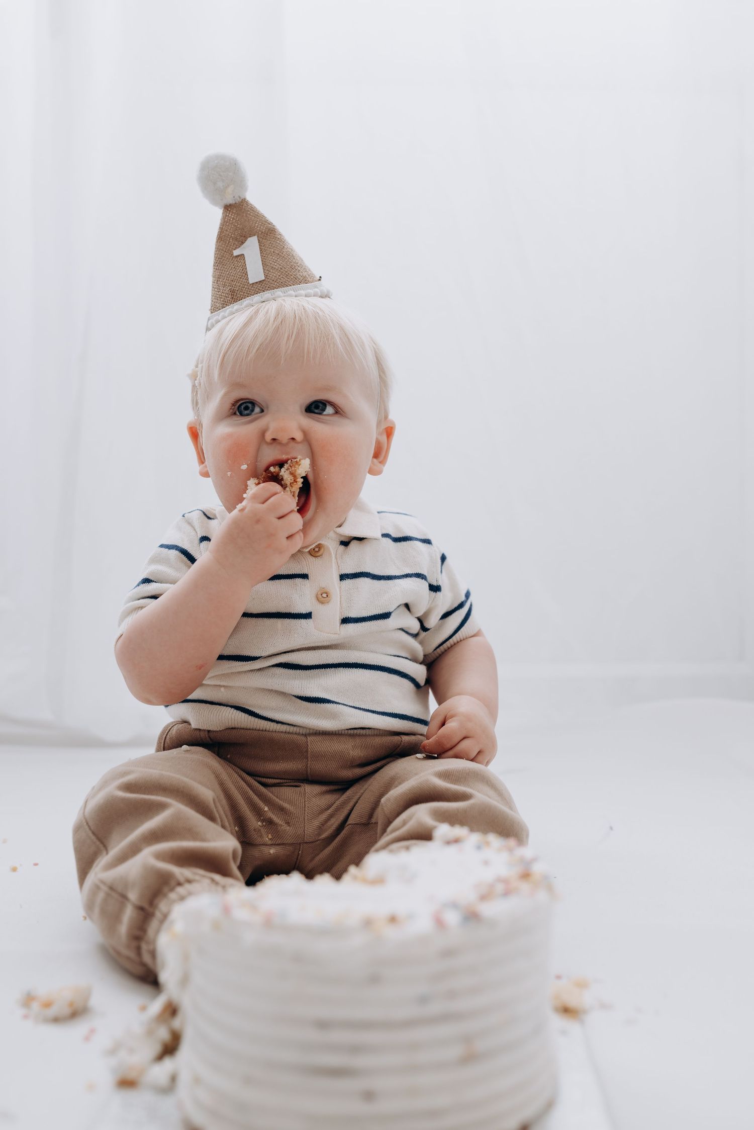 Baby in striped outfit enjoying their first birthday cake smash.