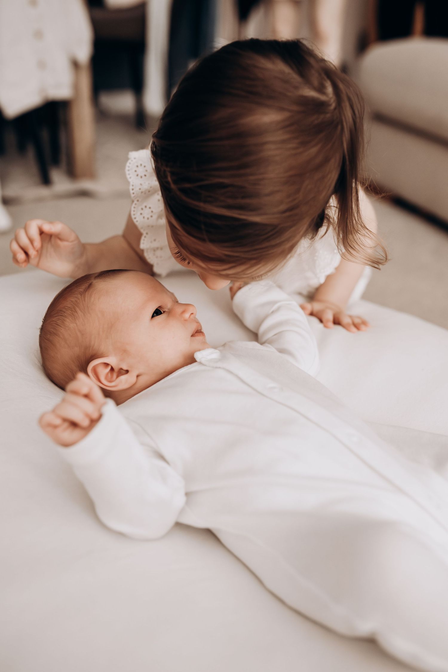Gentle interaction between sibling and baby in white clothing on light background.