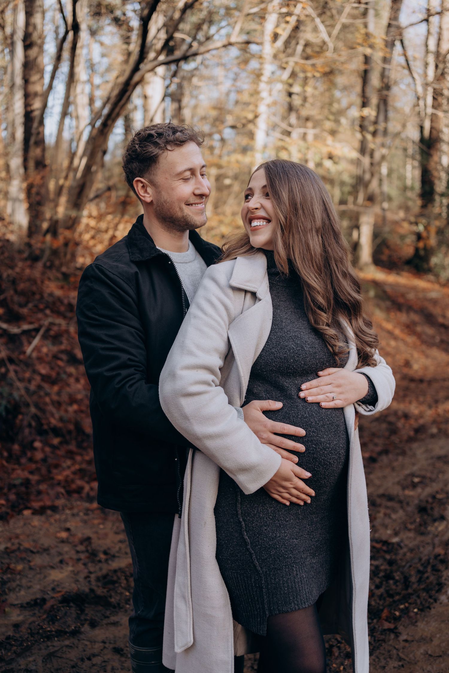 A couple embraces in a romantic autumn forest setting with fallen leaves and birch trees in the background.