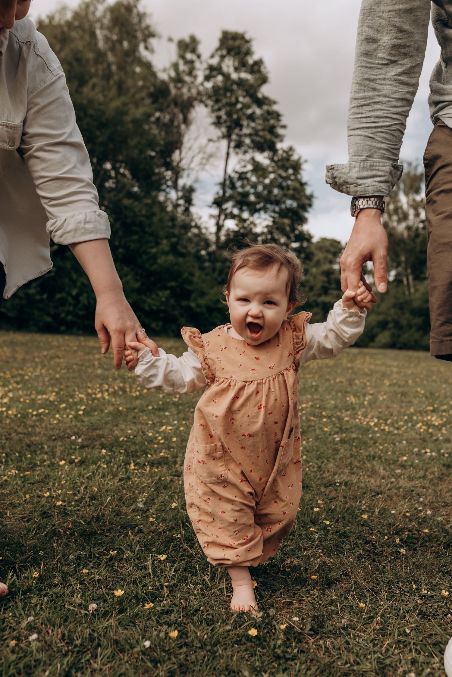 Baby in a peach-colored romper playing on grass with dandelions.