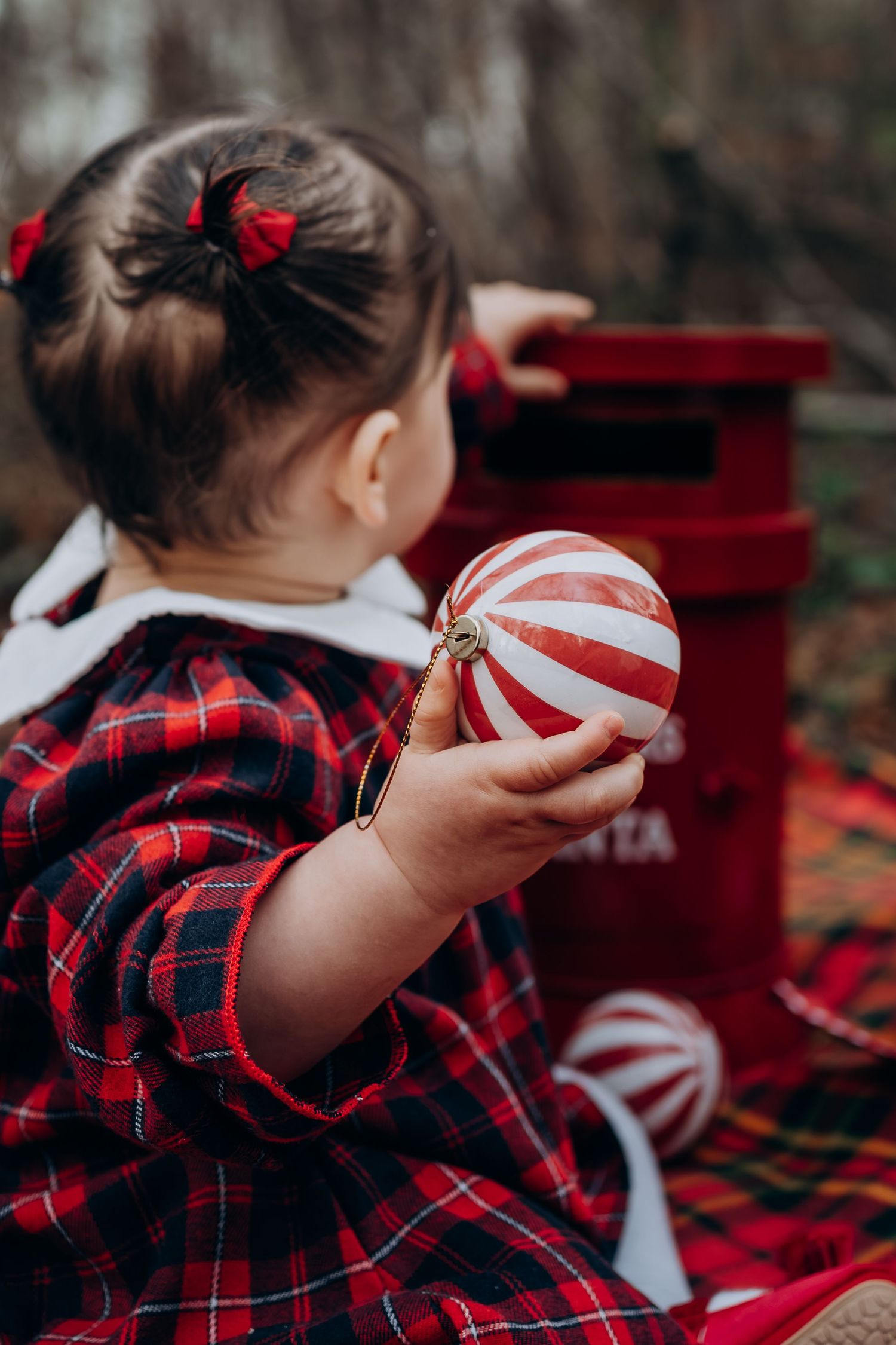 Person wearing red plaid shirt and hair bows in a festive holiday setting with red decor in background.
