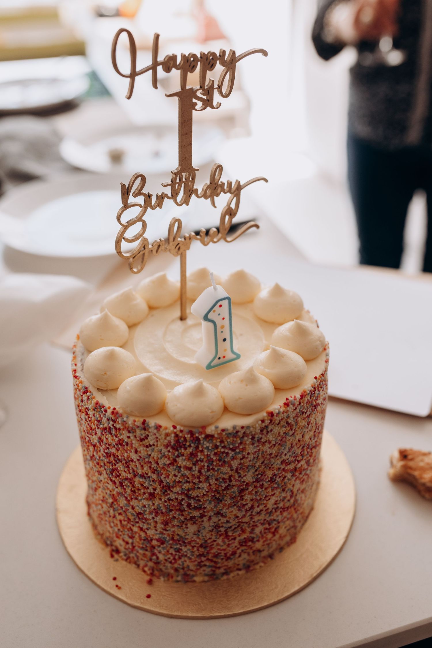 Birthday cake decorated with sprinkles and a gold topper displaying number one.