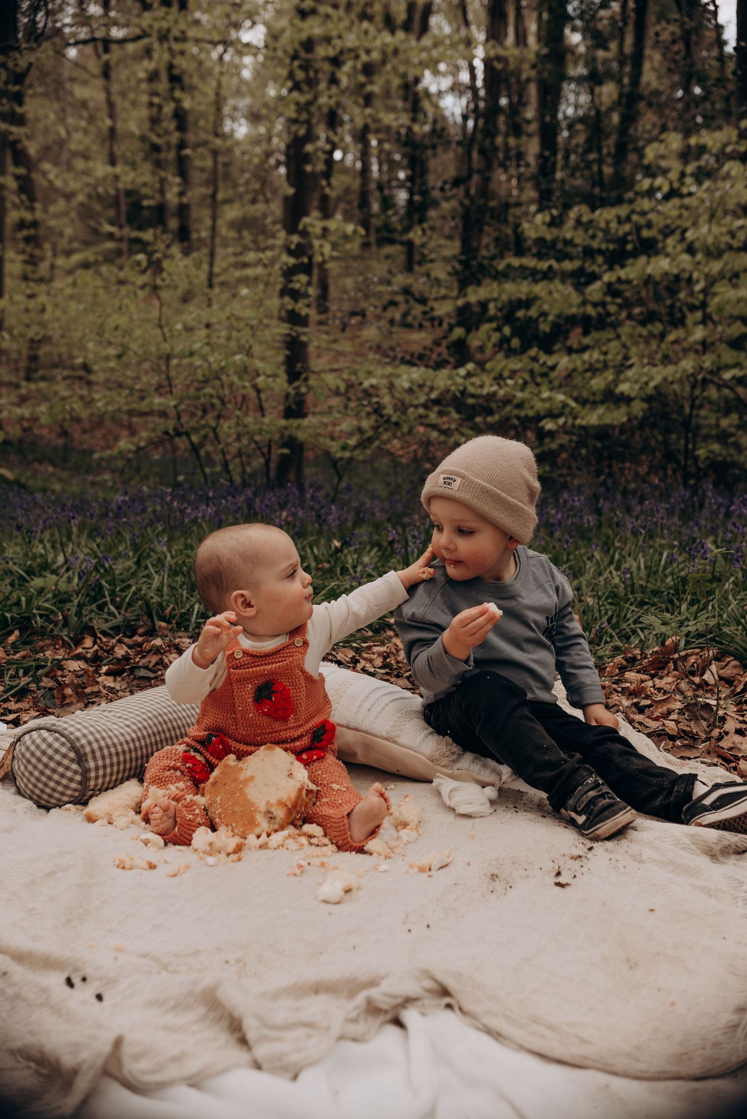 Children playing together on white blanket surrounded by autumn leaves in forest setting.