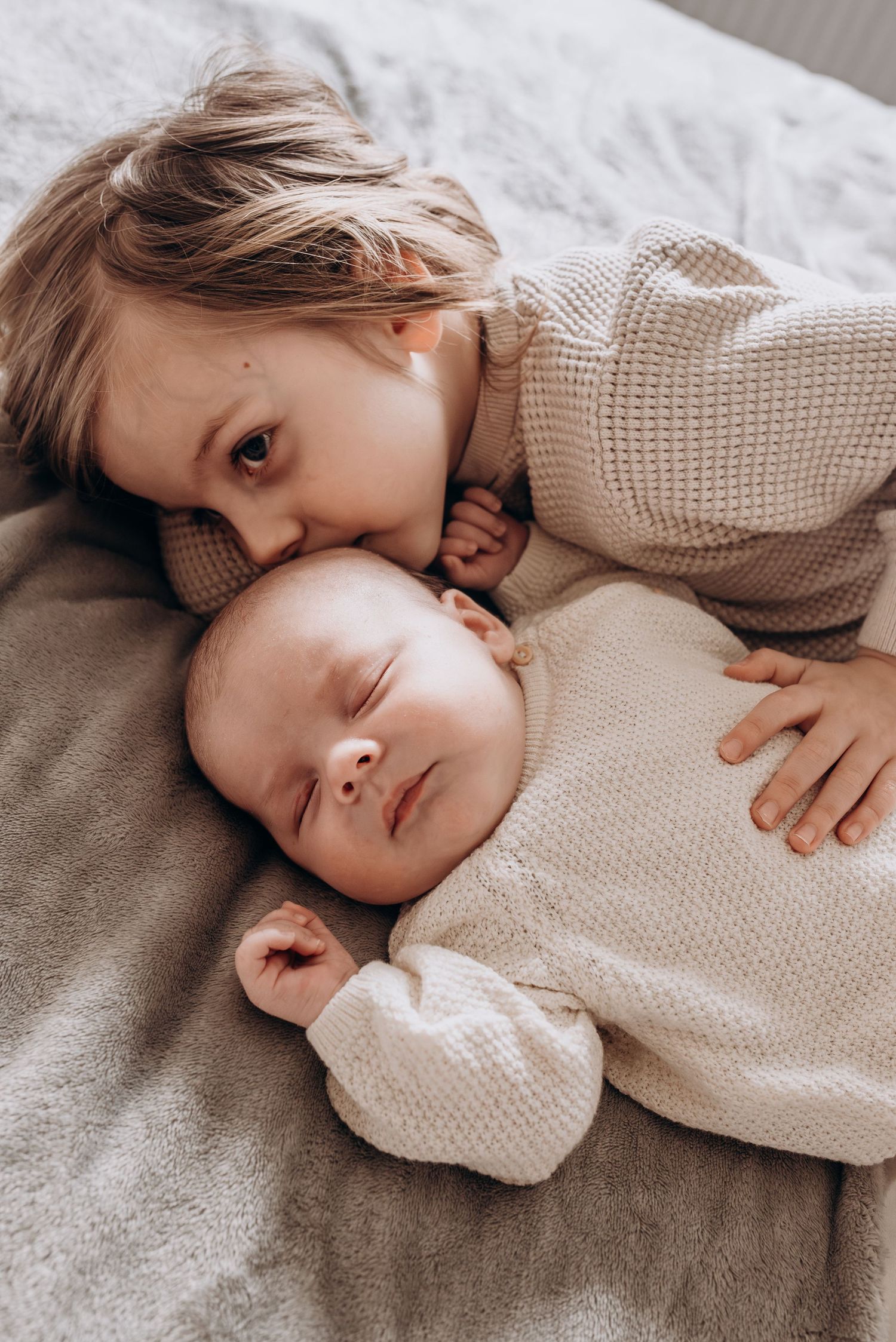 A sweet moment showing someone in a cream sweater cuddling with a baby on a soft gray blanket.