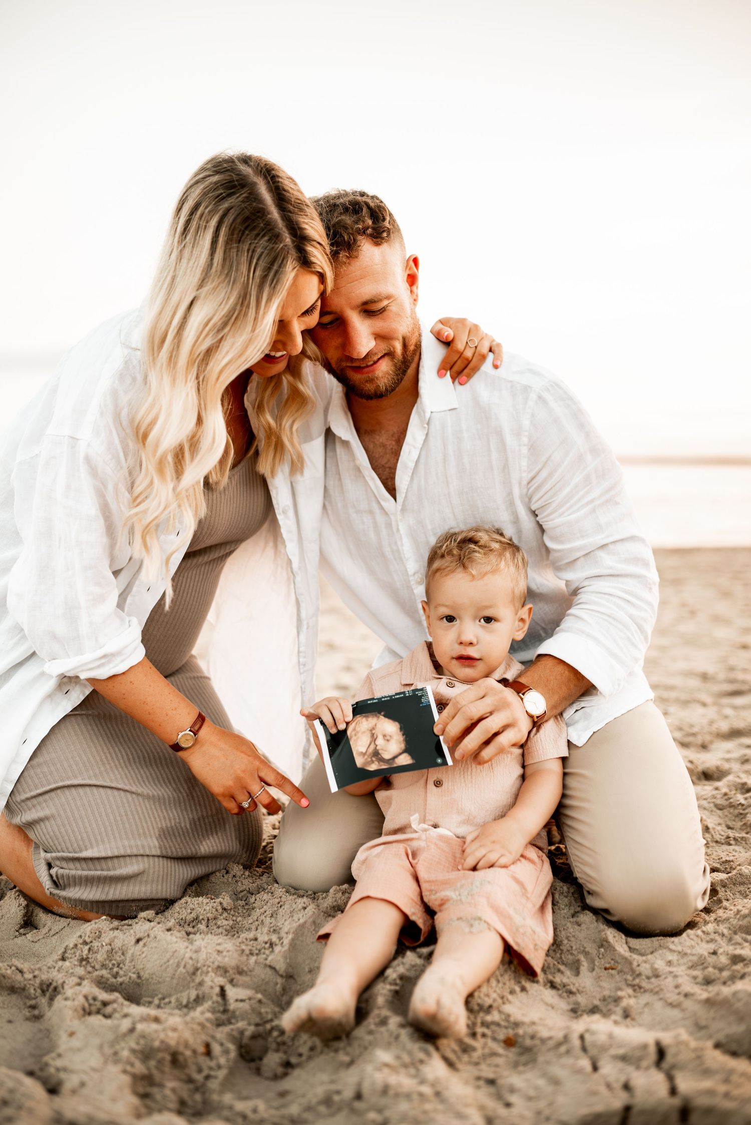 A family shares a tender moment on the beach while looking at an ultrasound photo.