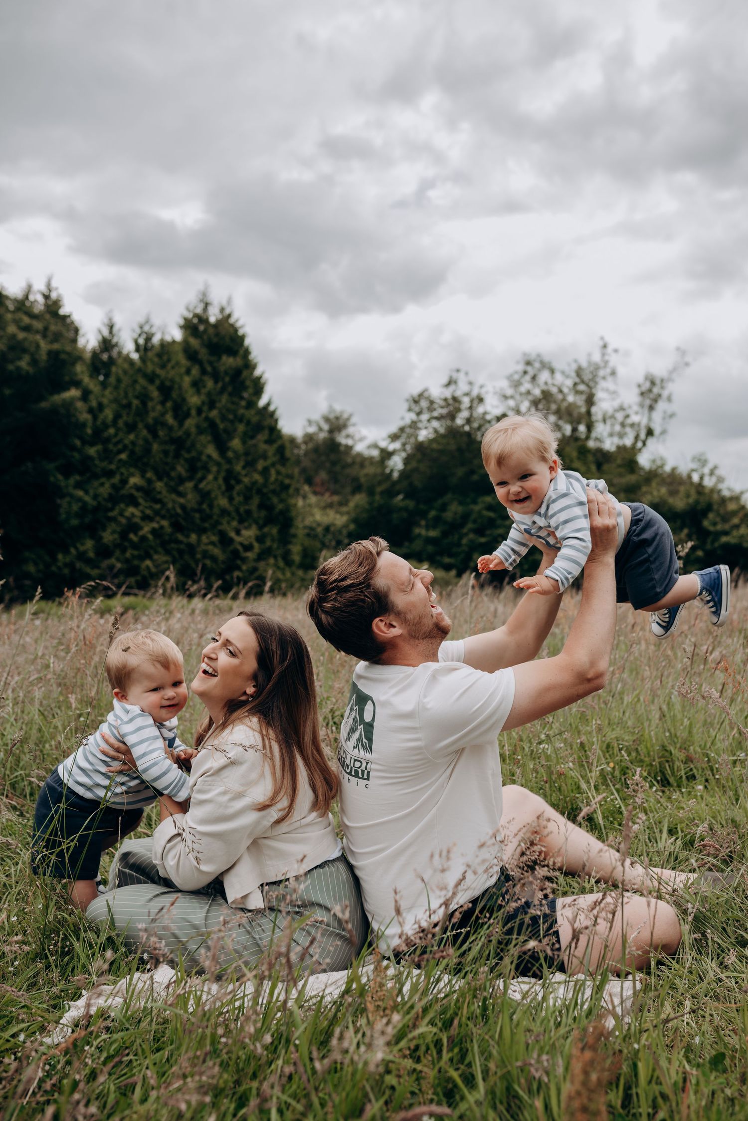 Family lying together in a grassy meadow on a cloudy day.