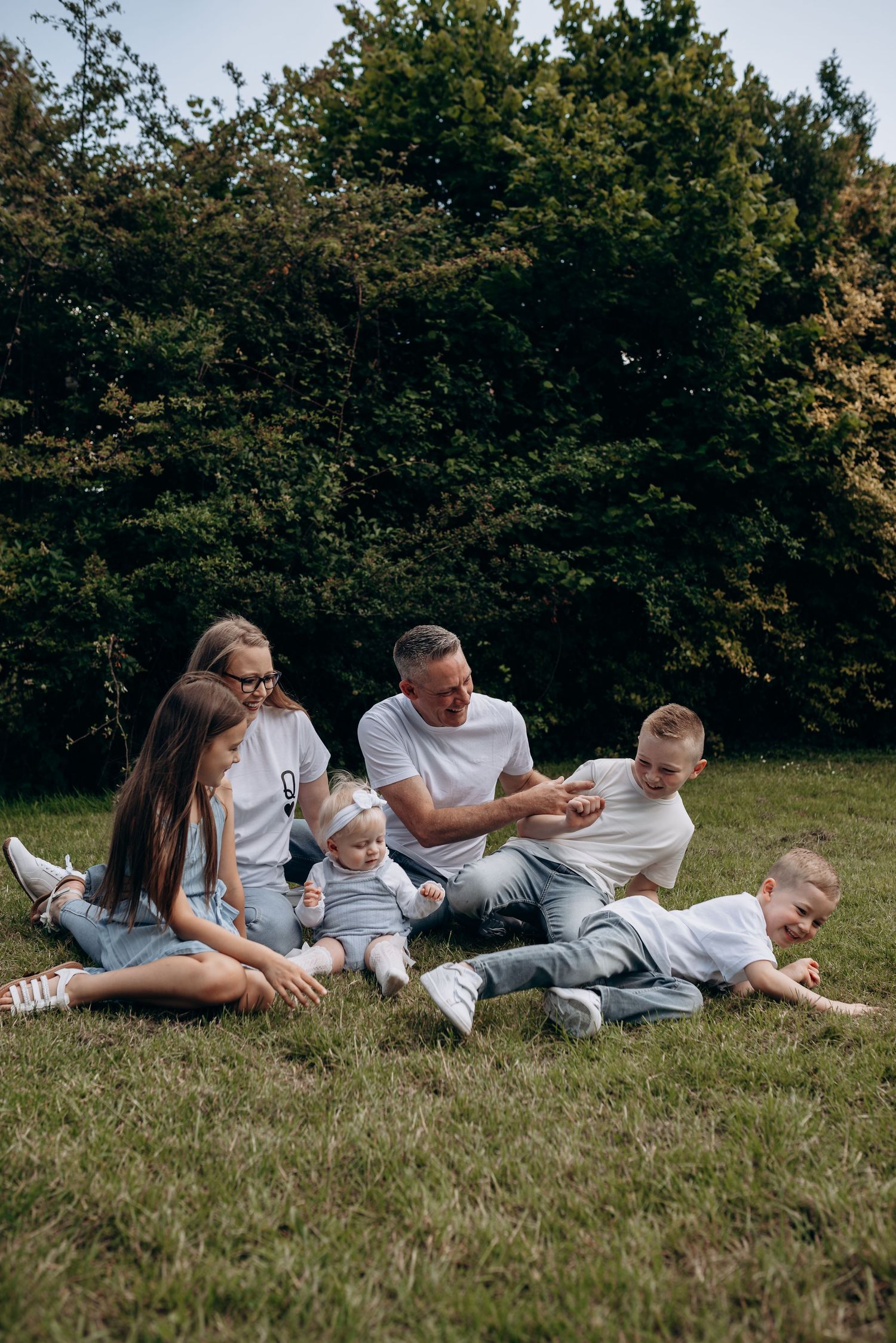 Family relaxing together on grass in a park setting during a sunny day.