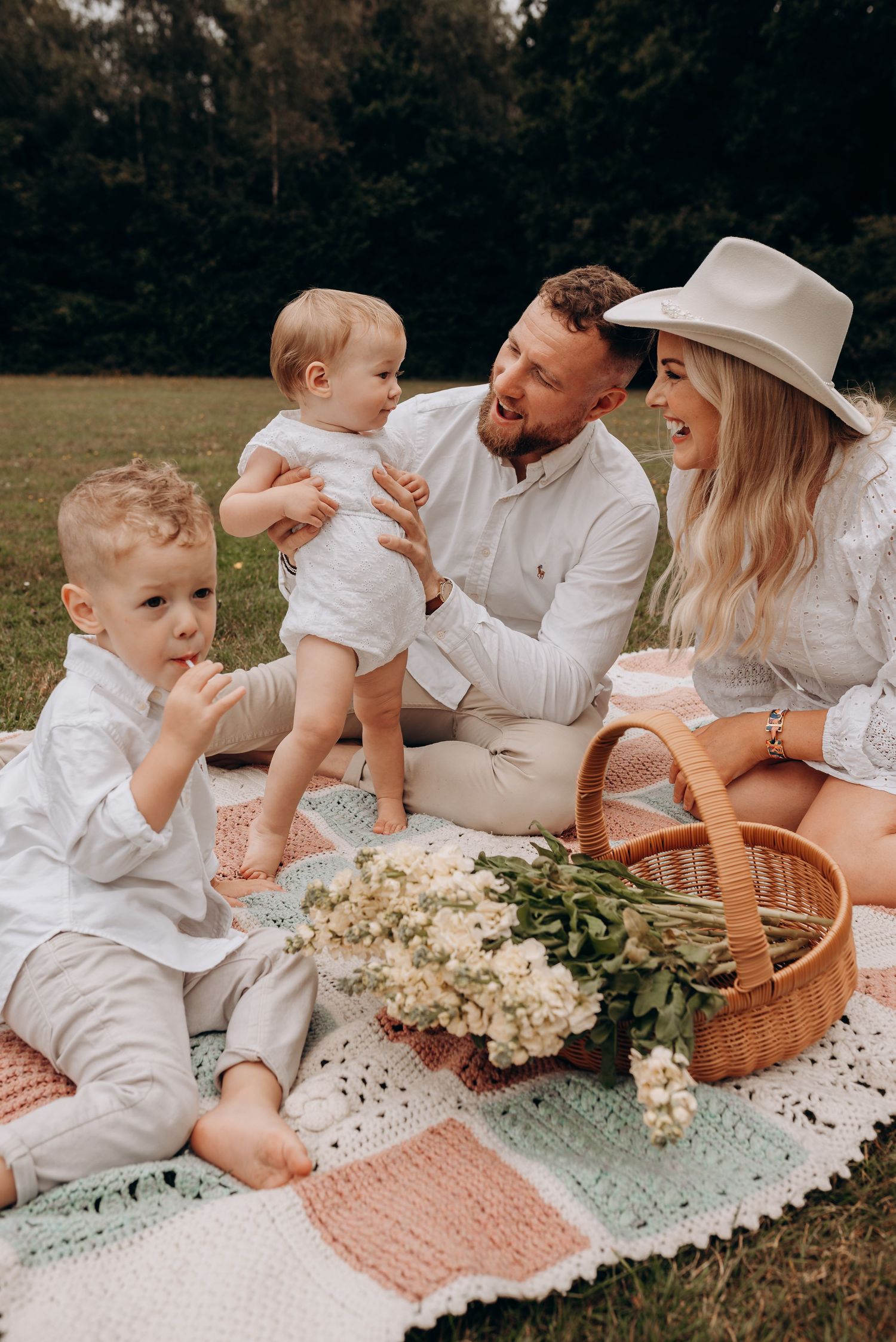 A family enjoys a picnic on a blanket with flowers and a wicker basket in a sunny field.