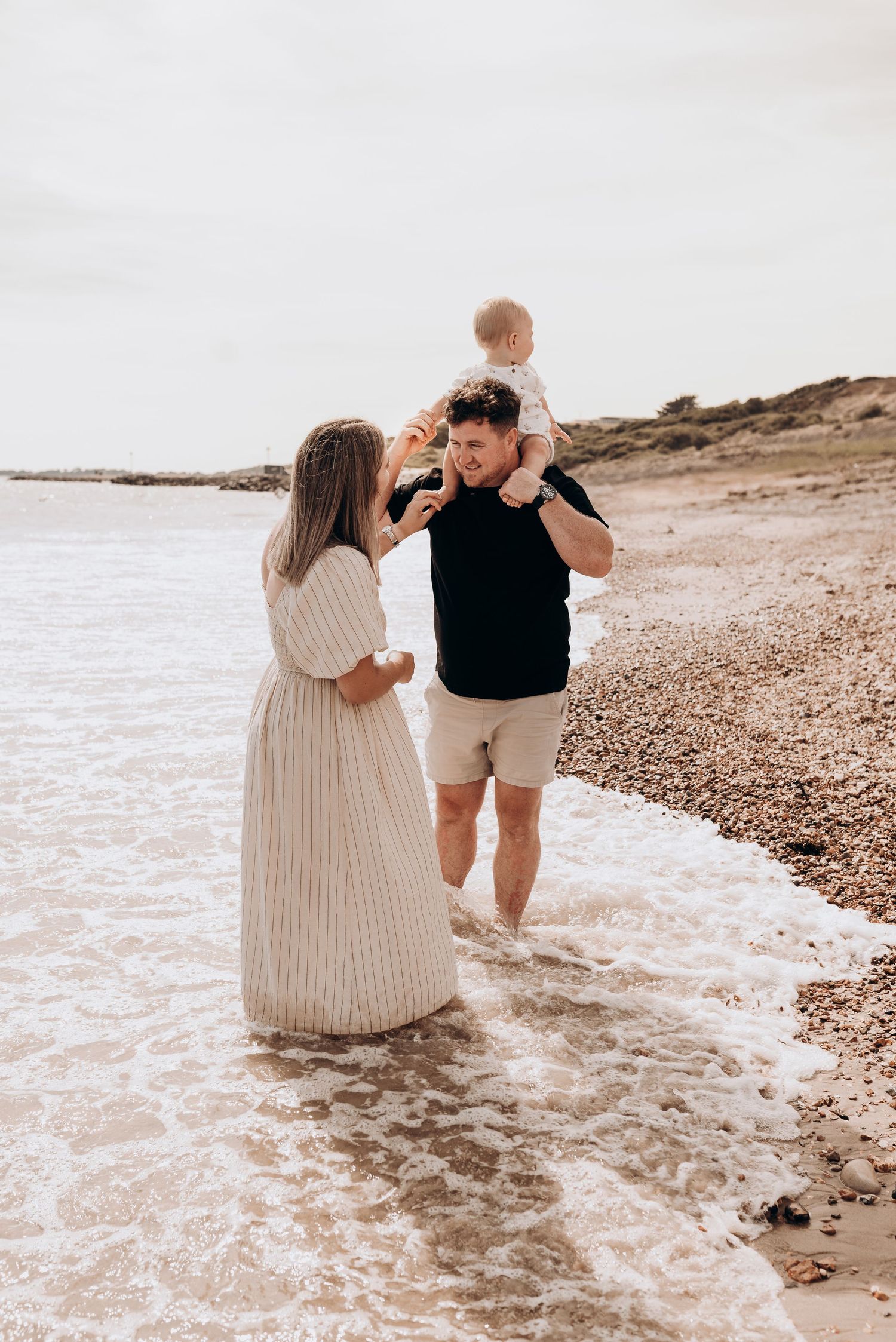 A family plays together at the beach as waves lap at their feet.