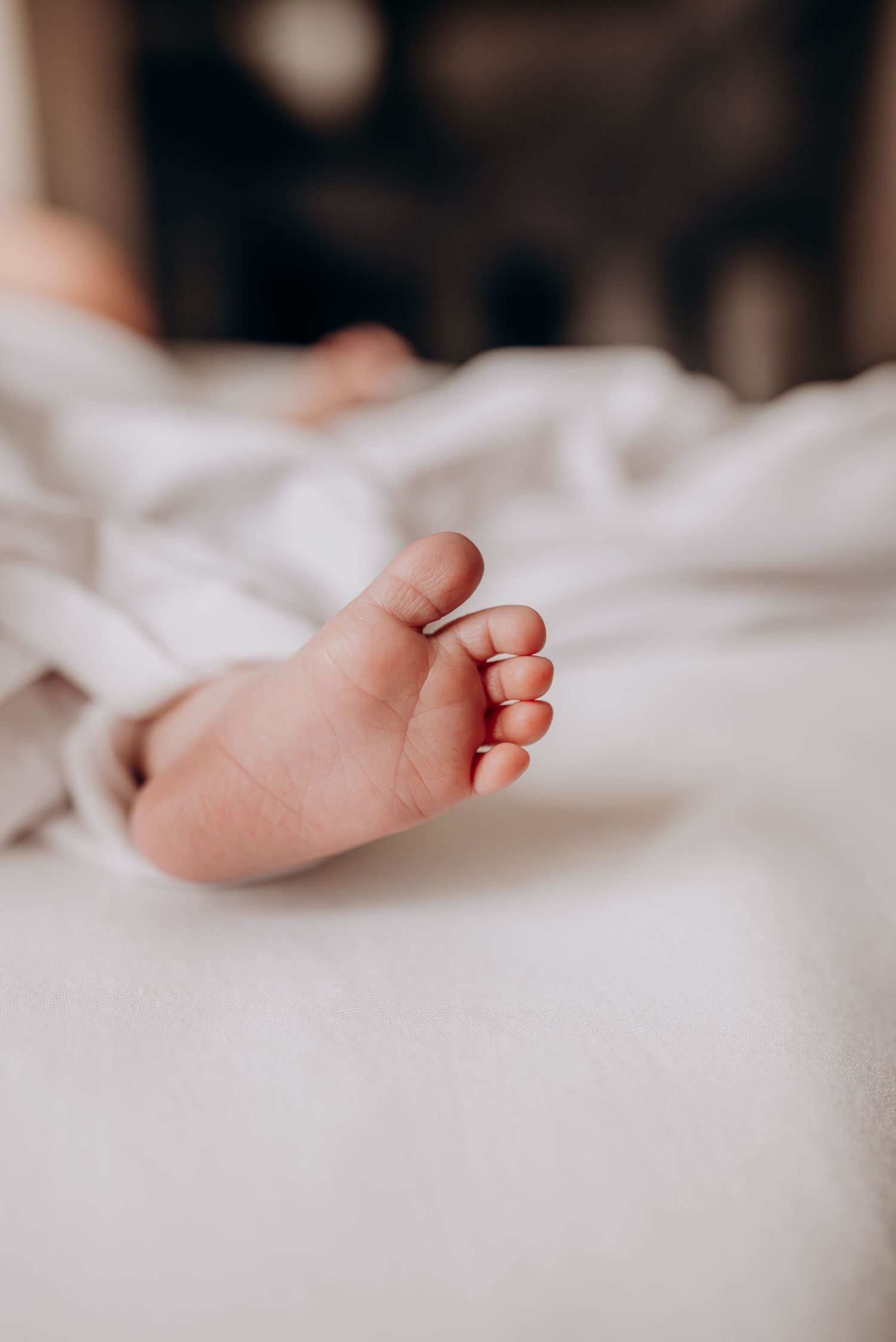 Close-up of tiny newborn baby feet wrapped in soft white blankets.