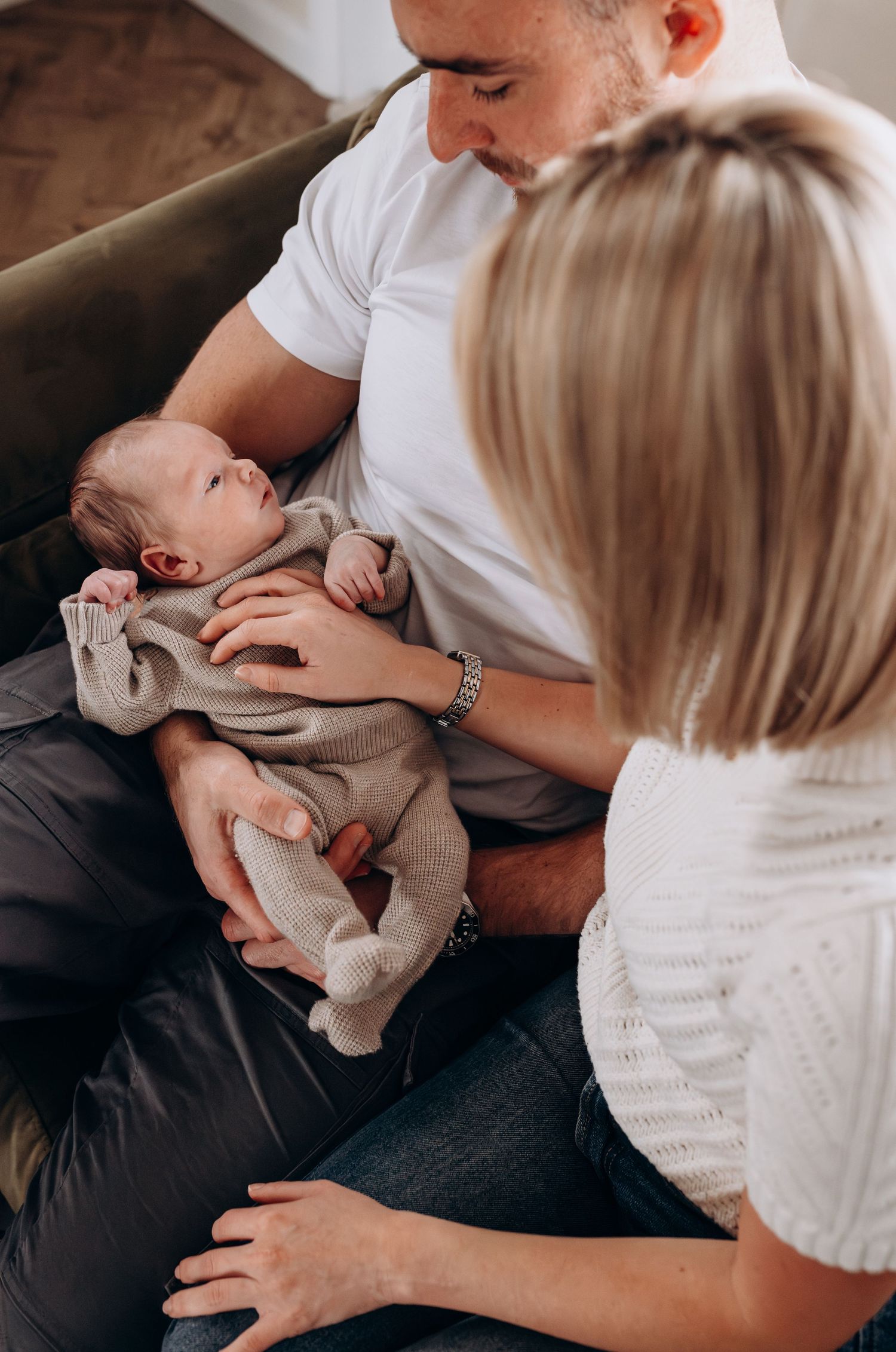 Parents on couch tenderly holding and interacting with their newborn baby.