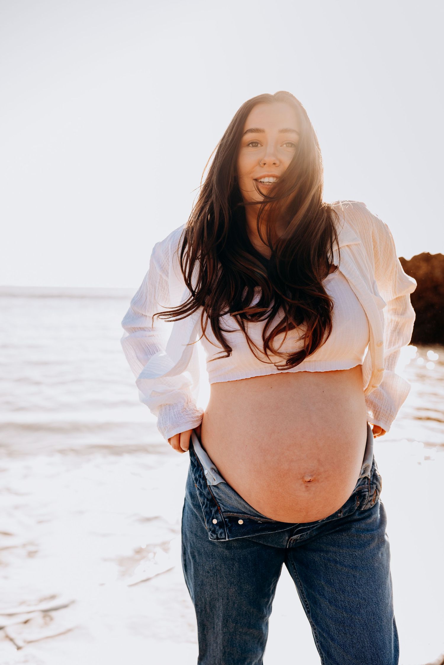 Maternity photo series showing pregnant woman in white shirt and jeans at sunset on beach.