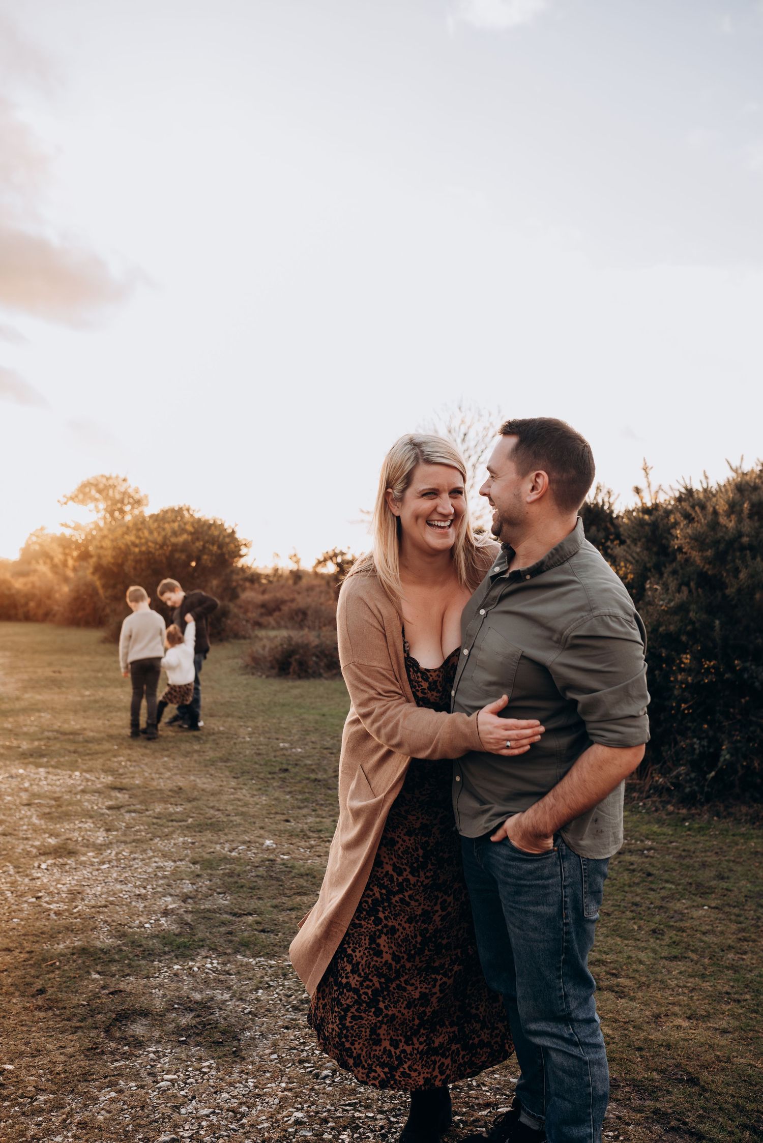 A couple shares joyful laughter and embraces in an outdoor setting during golden hour.
