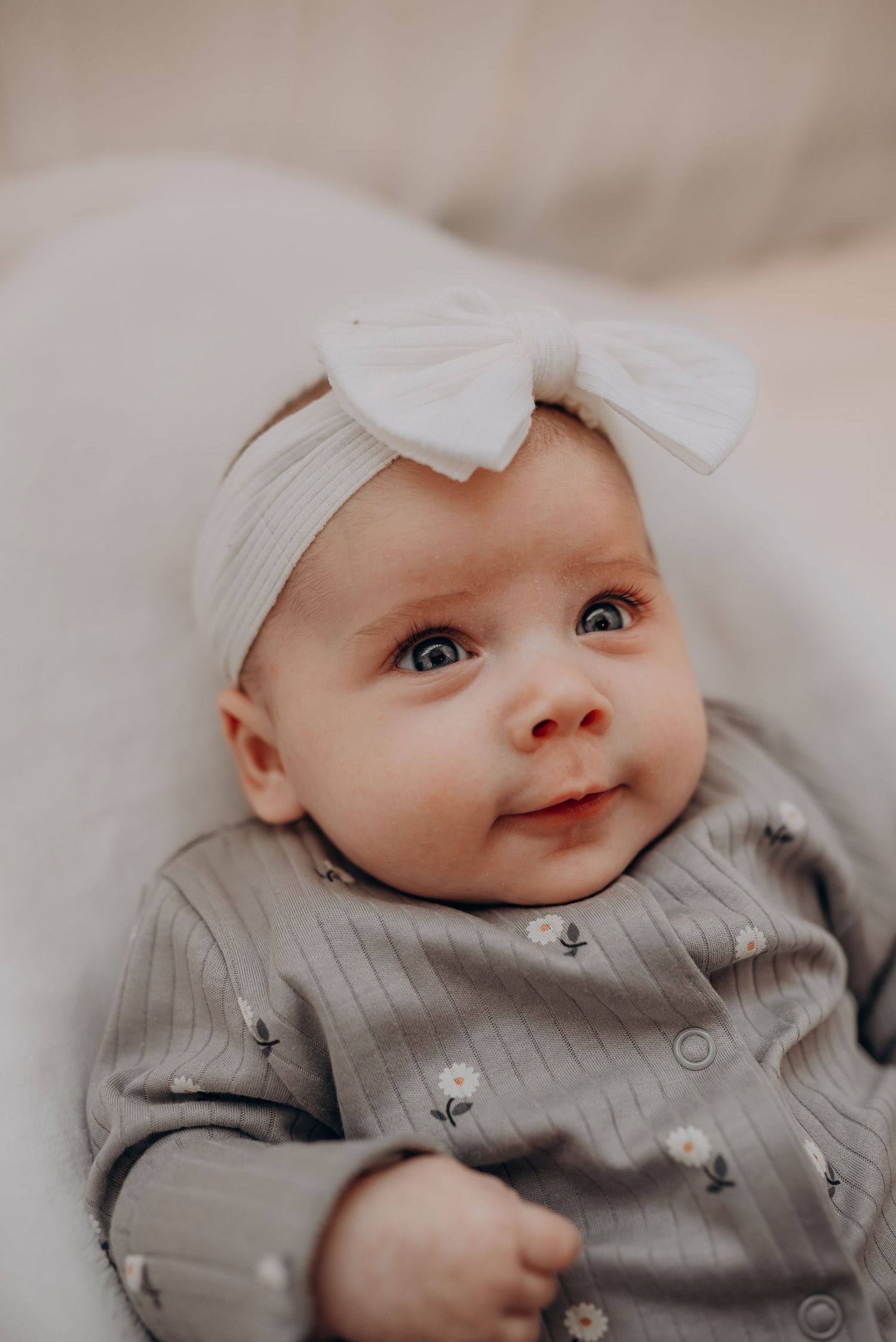 A baby wearing a gray outfit and white bow headband smiles sweetly.