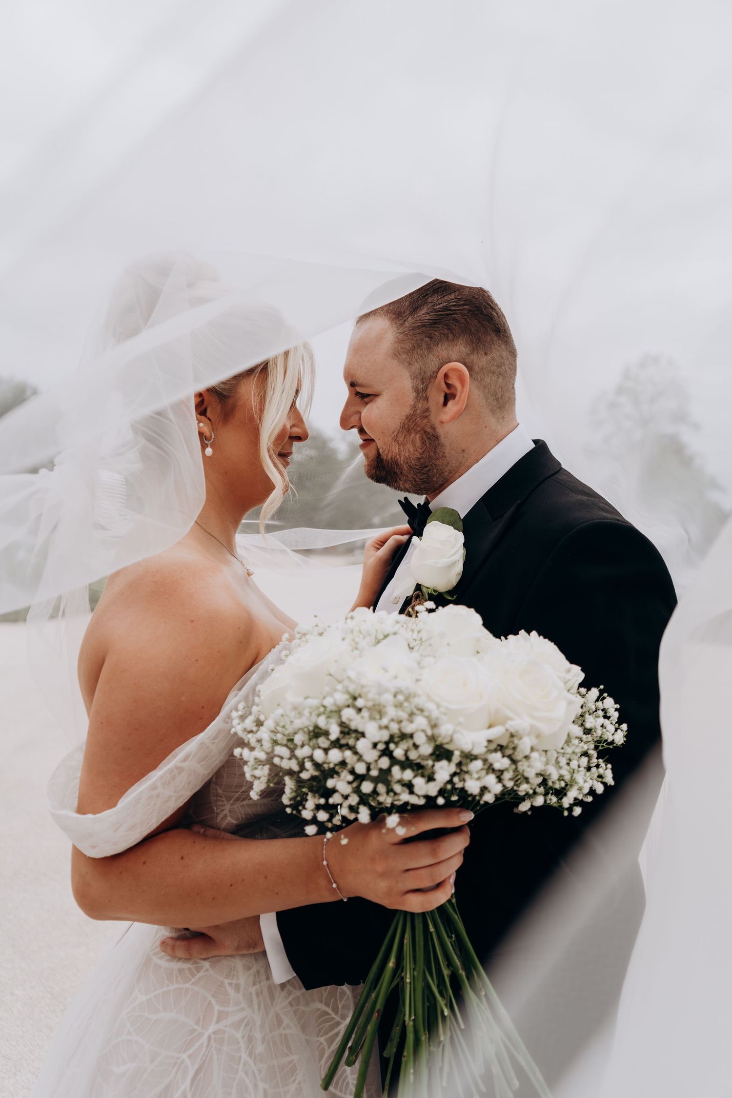 Romantic wedding portrait with couple holding beautiful white baby's breath bouquet against soft ethereal backdrop.