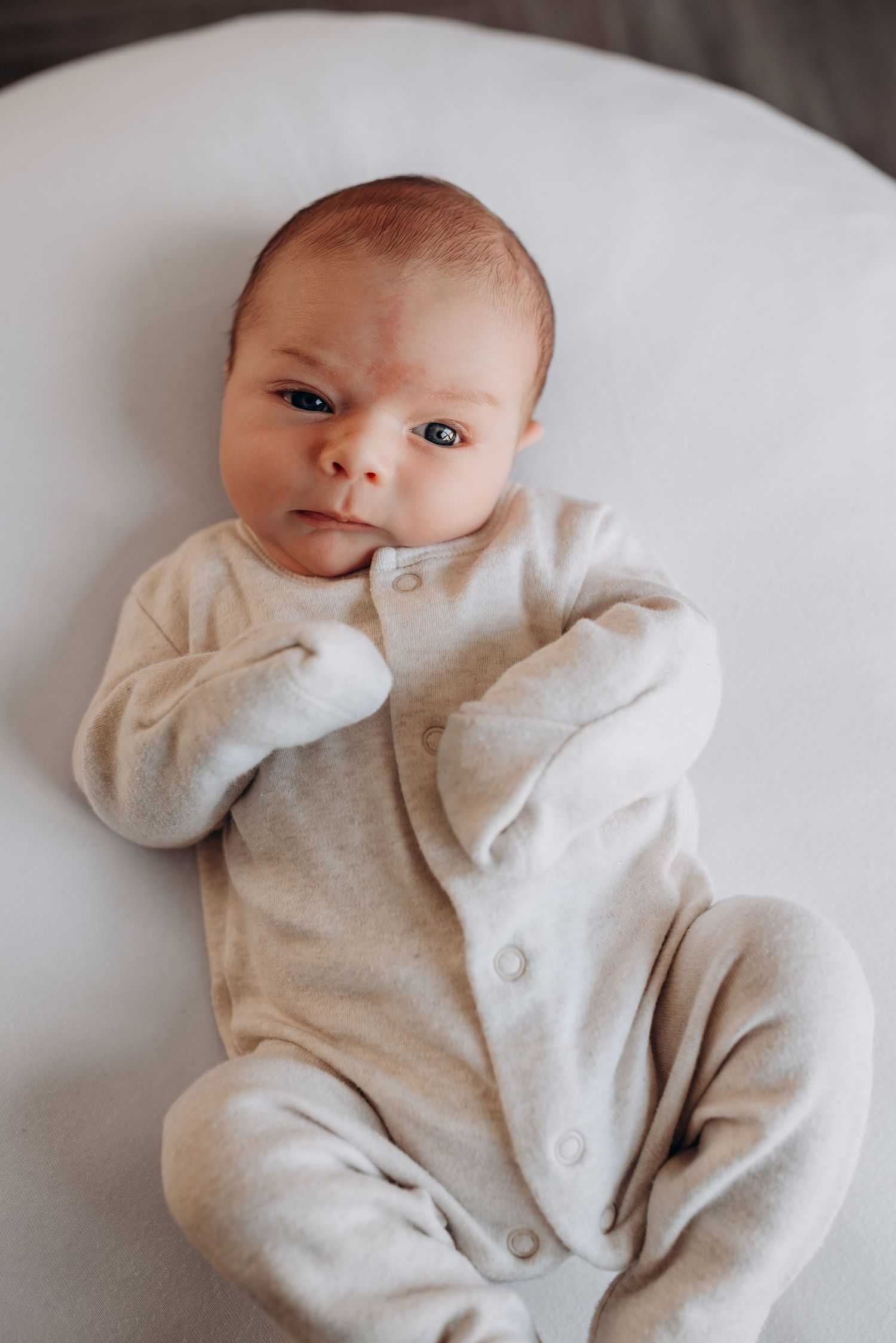 Baby in light gray onesie lying on white surface showing various expressions.