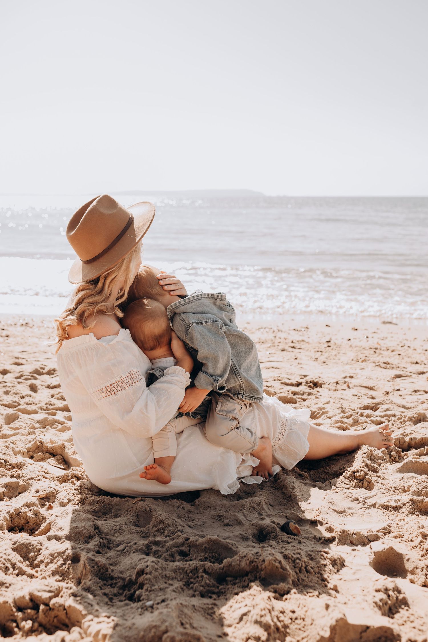 Intimate beach moment captured with brown hat and neutral tones on sandy shore.