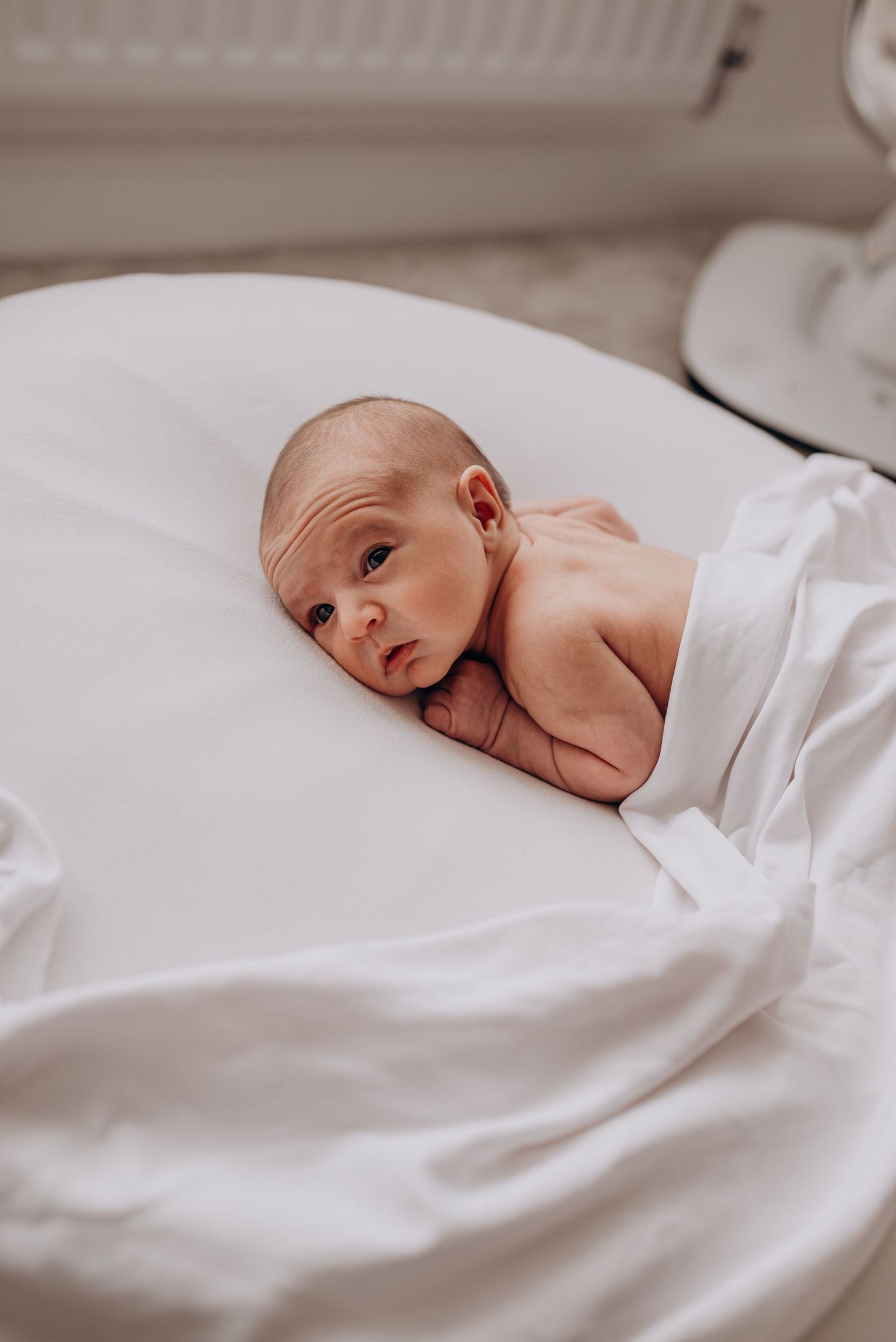 Newborn baby wrapped in white blankets lying on white bedding.