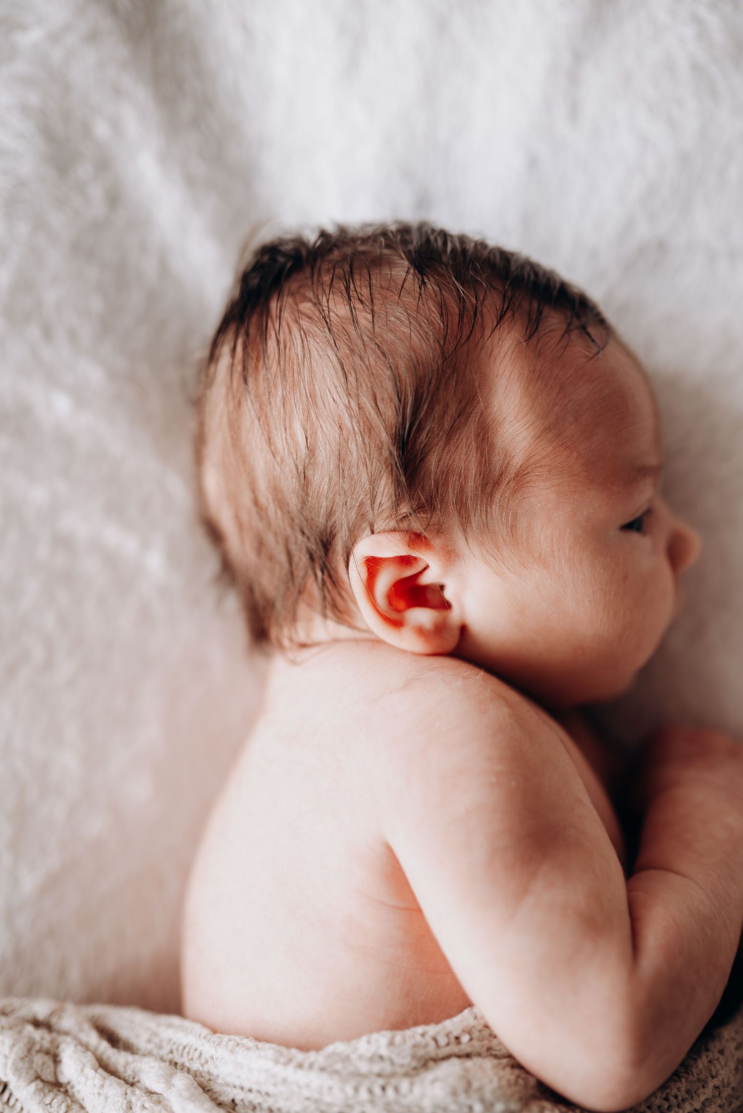 Side profile views of sleeping newborn baby on white textured background.