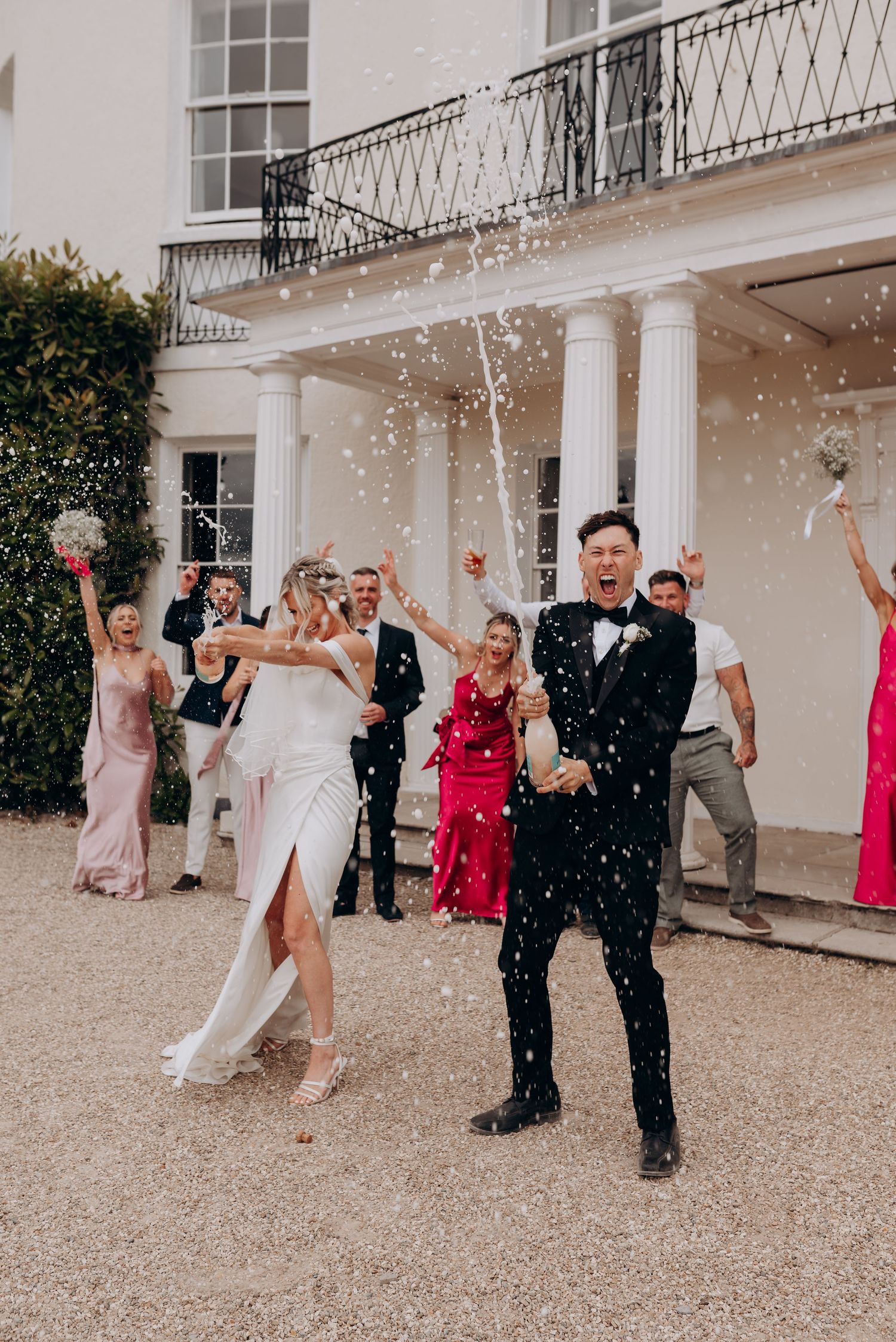 Wedding party celebrating with confetti throws outside an elegant white building.