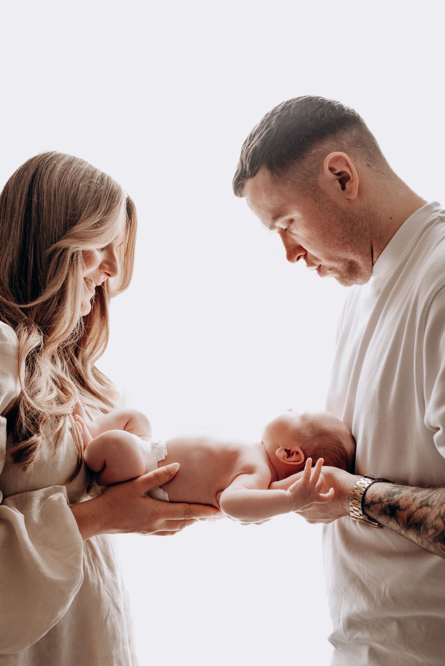 Parents sharing tender moment with their newborn baby in bright white room.