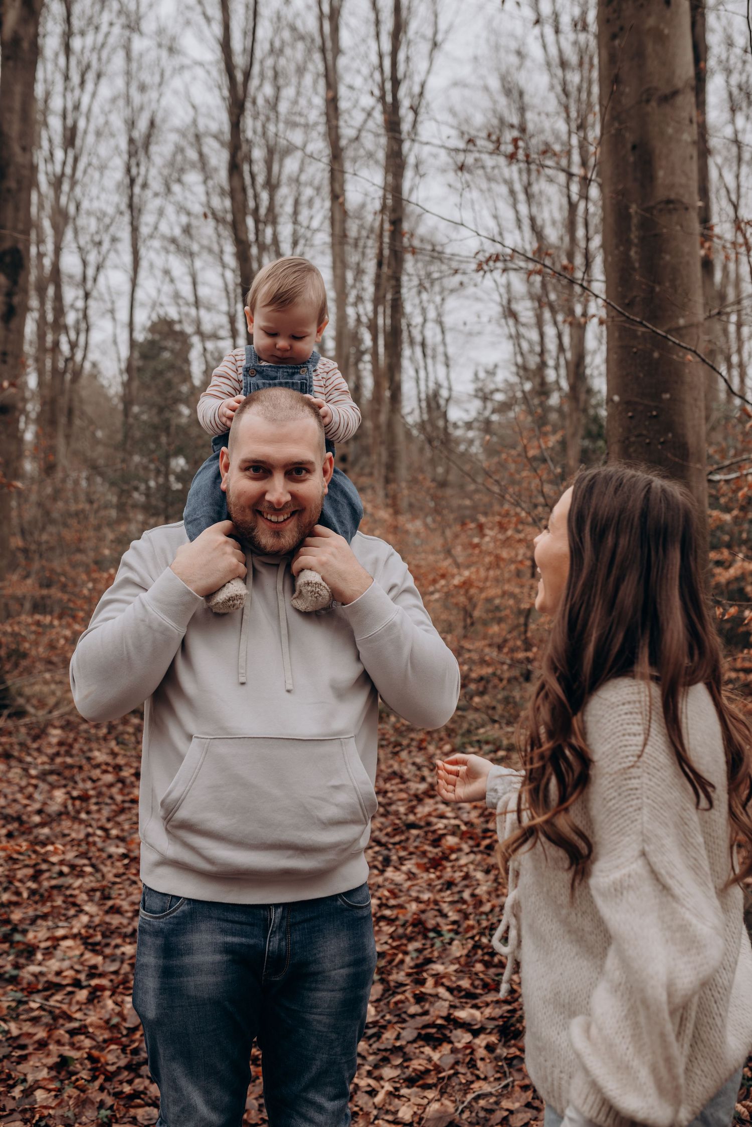 Playful family photoshoot in an autumn forest with fallen leaves.