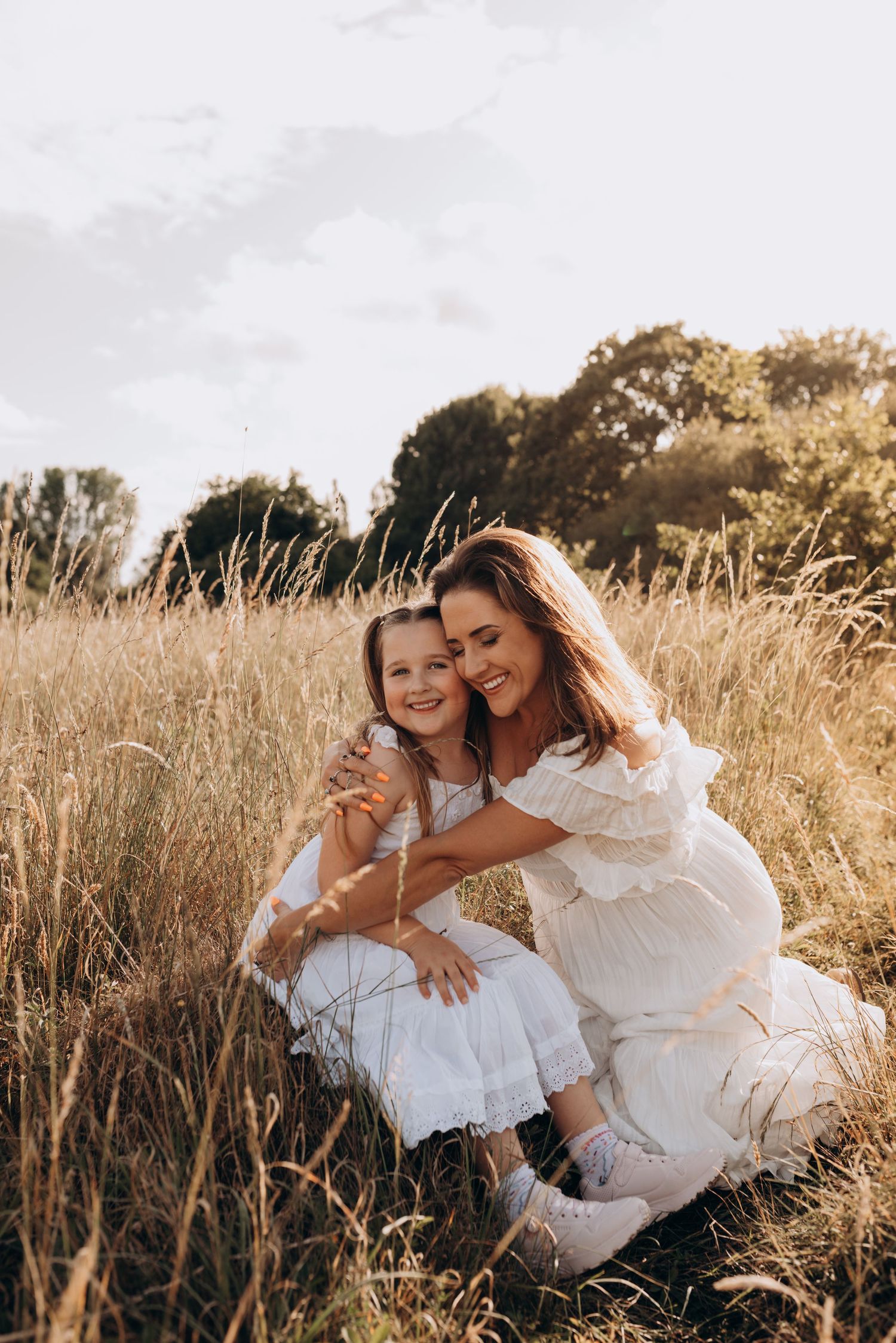 A tender moment captured in a sun-drenched field of tall grass with warm golden light filtering through the scene.