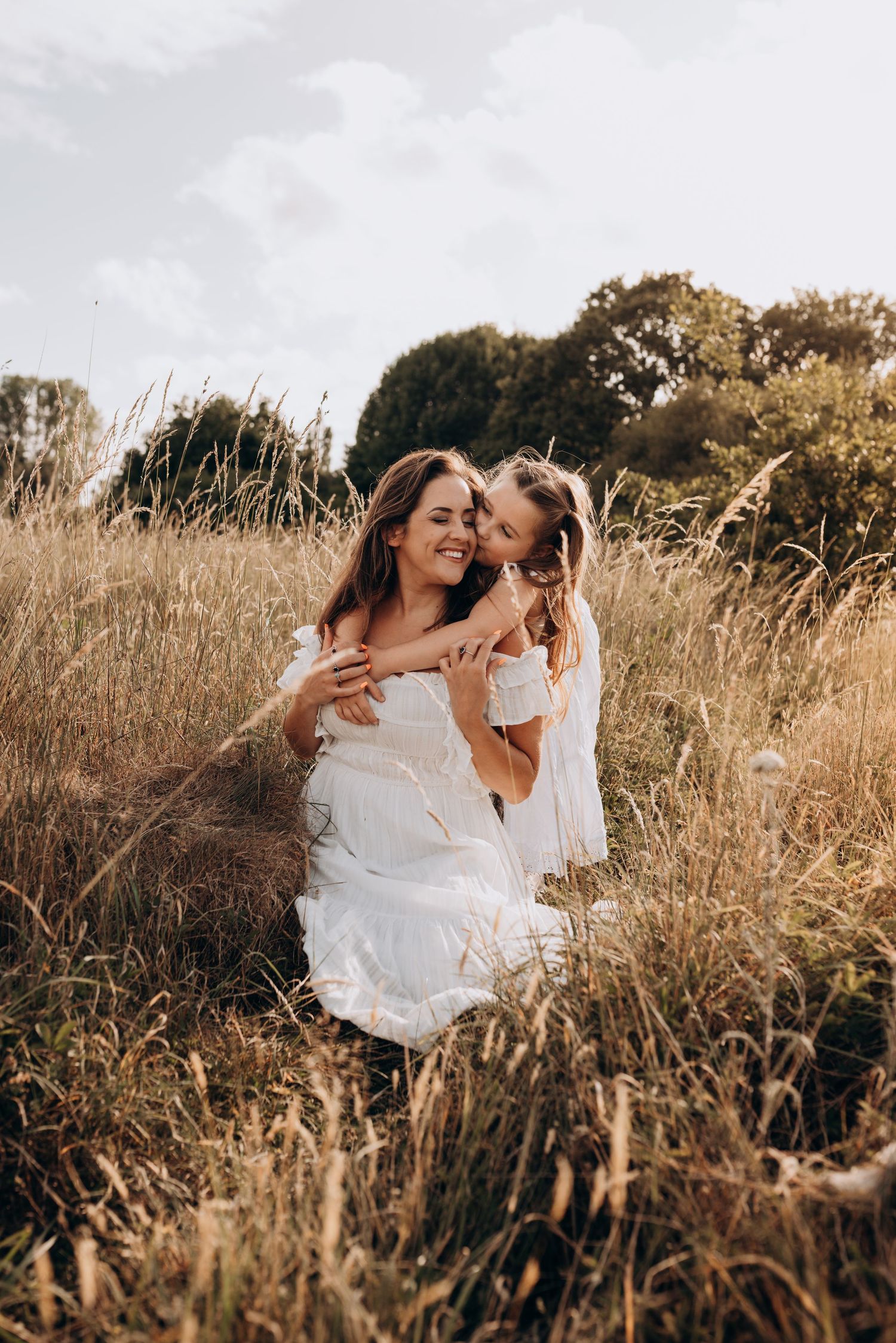 A mother and child share joyful moments together in a golden sunlit field of tall grass during sunset.